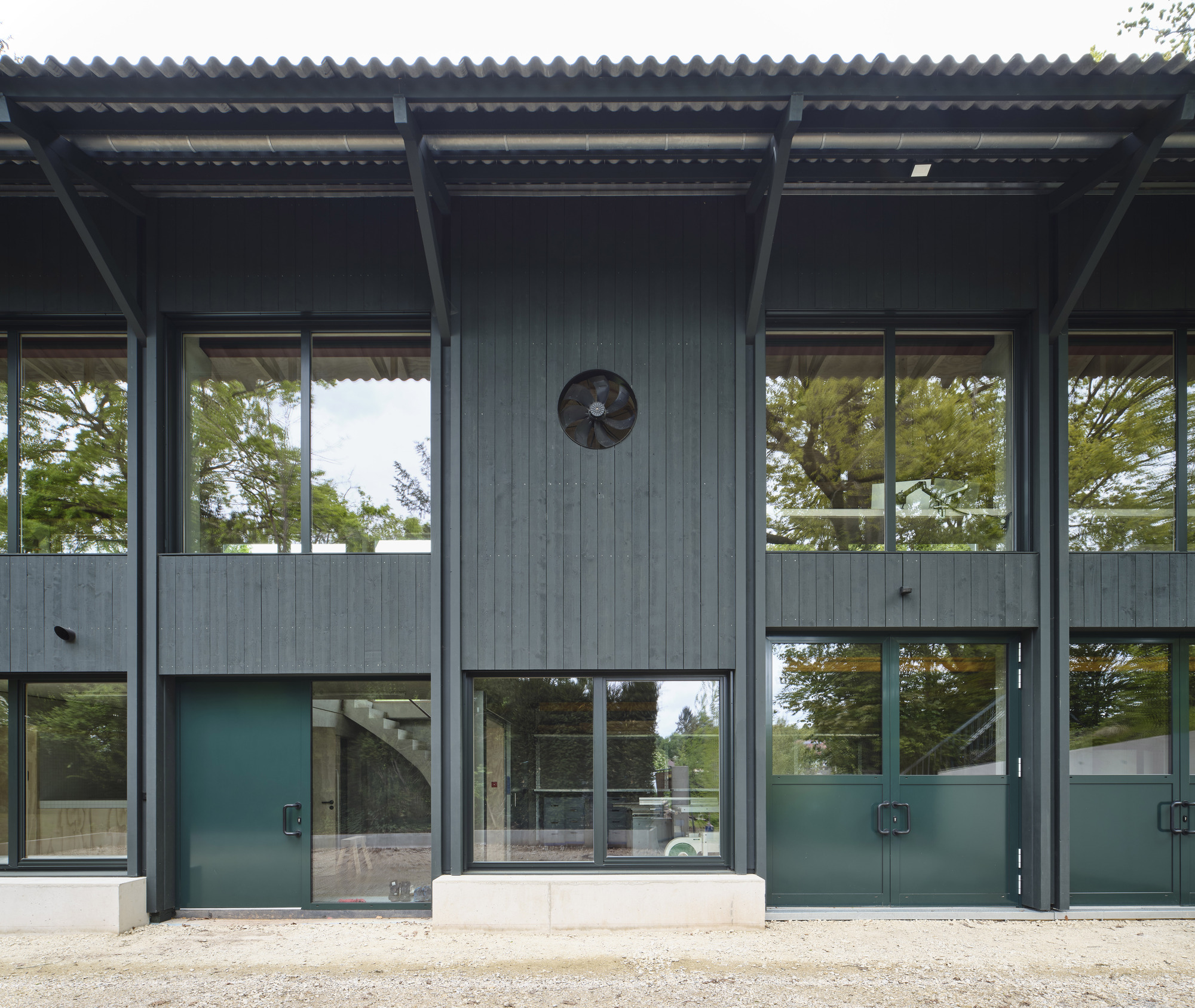 Facade with corrugated metal roof overhang and large glazed panels separated by teal-painted steel doors