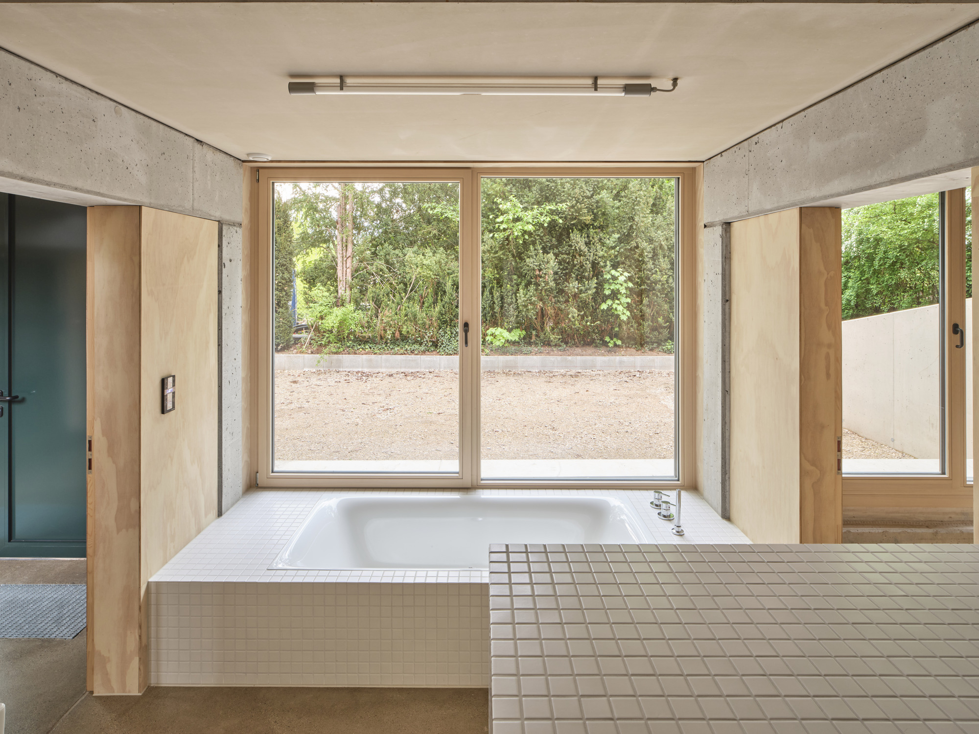 Bathroom with white tiled bathtub platform facing full-height glazed doors to exterior gravel garden