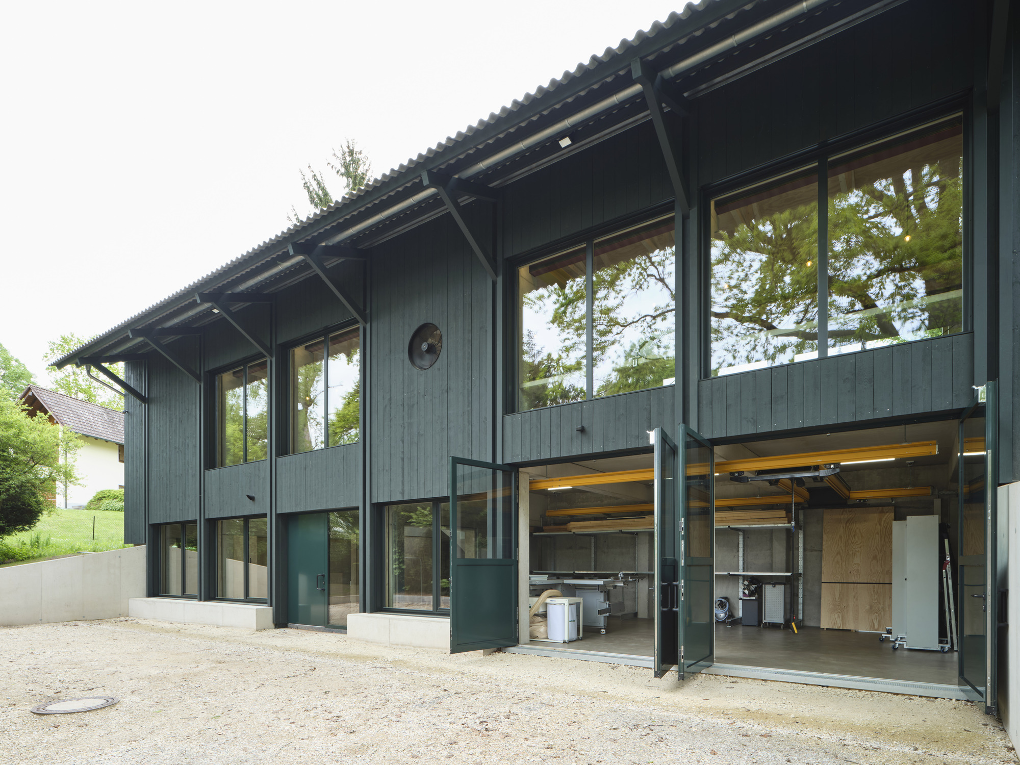 Two-story timber facade with exposed corrugated overhang and open garage doors revealing workshop equipment
