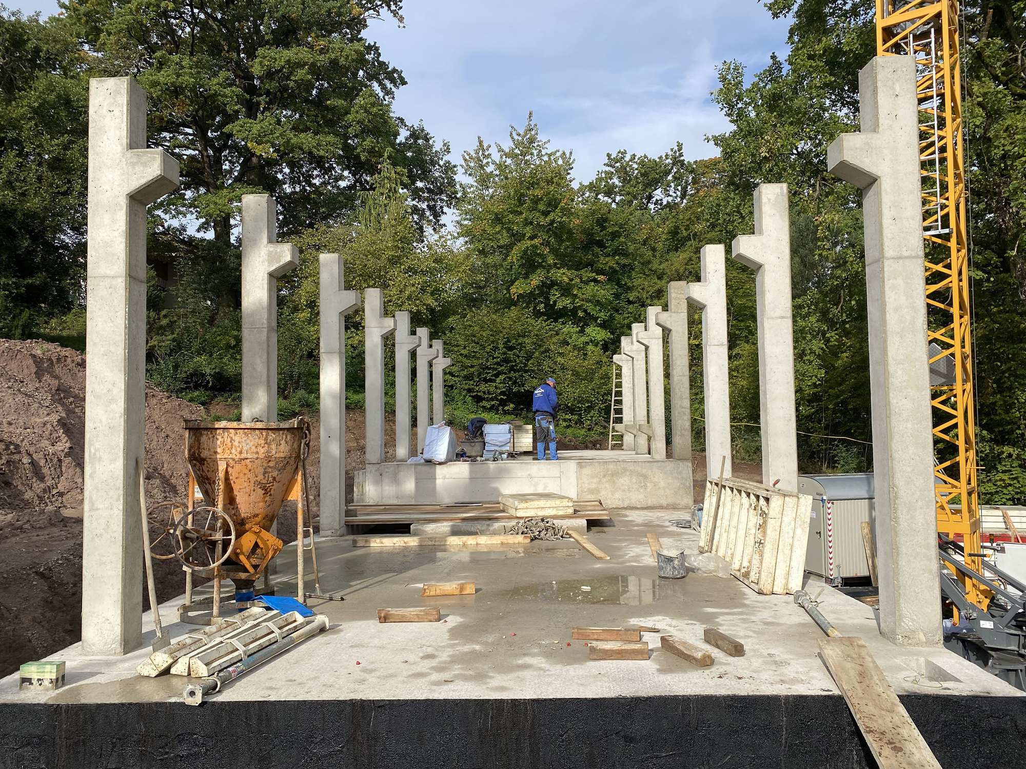 Construction site showing rows of precast concrete columns set into a concrete slab with a yellow crane visible