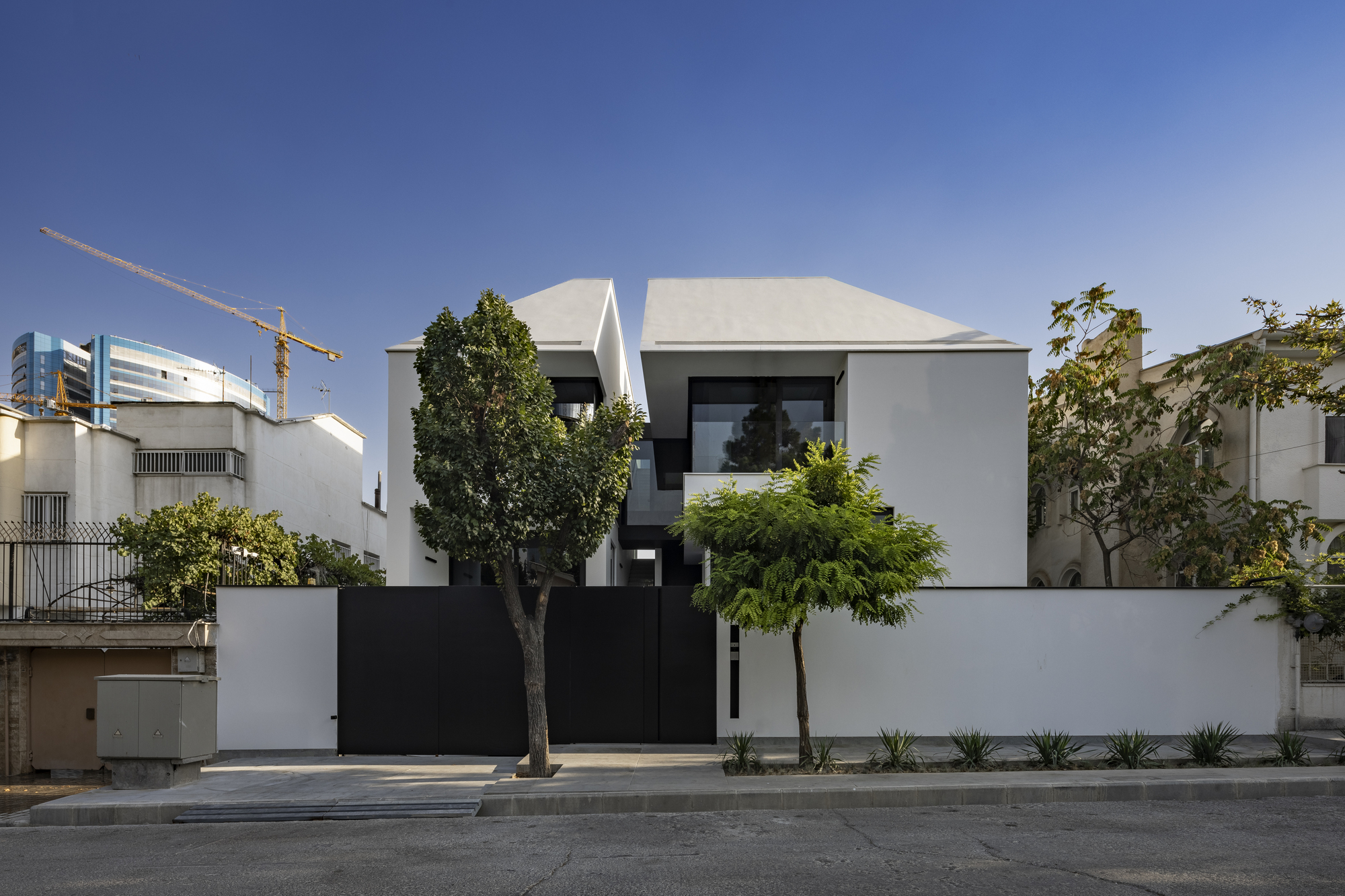 Street view of the white stucco facade with black metal gate and planted trees along the sidewalk
