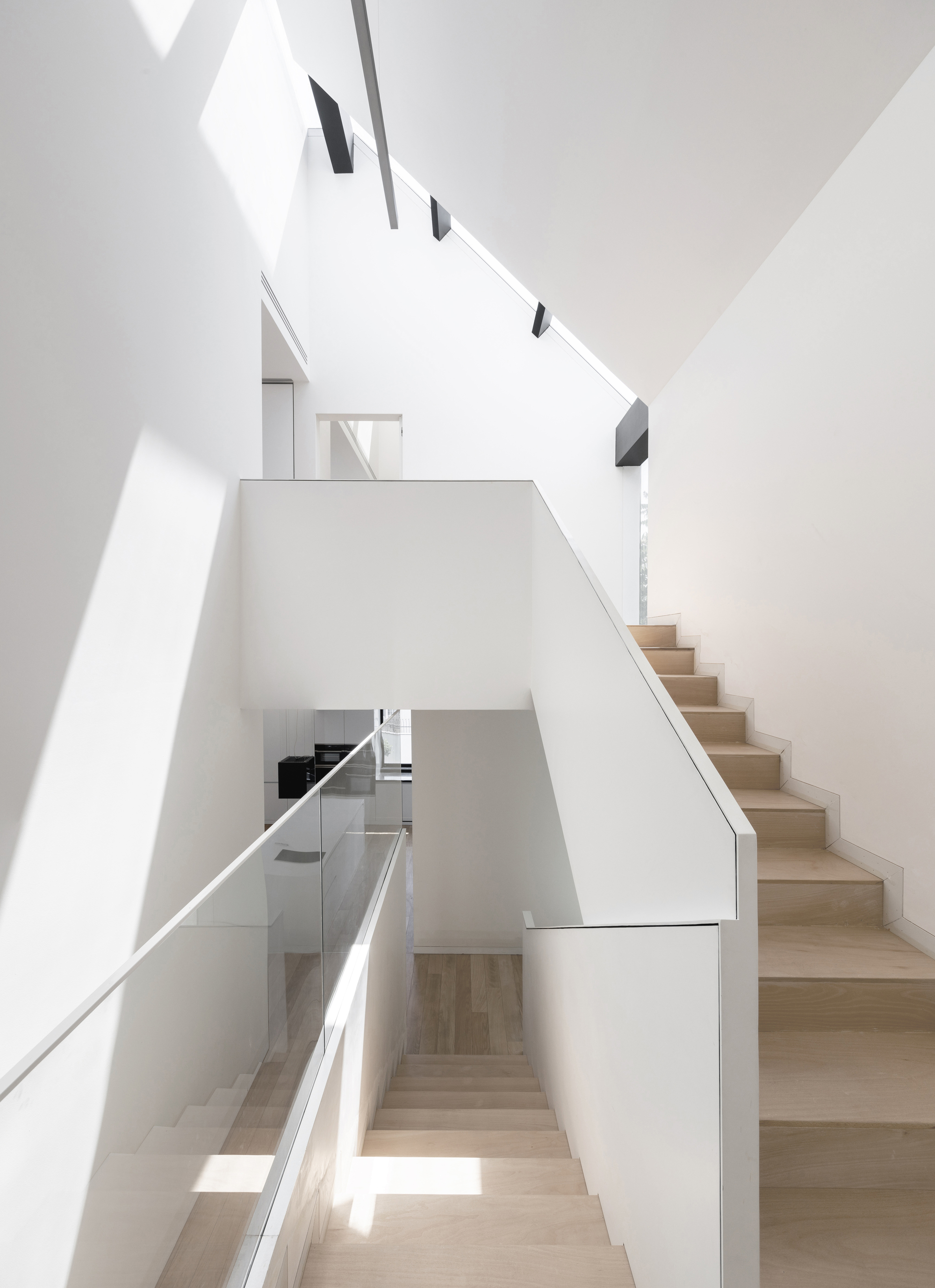 Multi-level staircase with light wood treads and white walls flooded with natural light