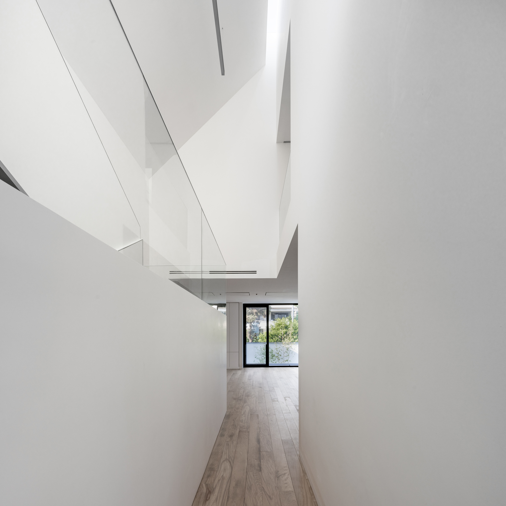 Corridor with angled white walls and skylights leading toward a glazed door with garden beyond