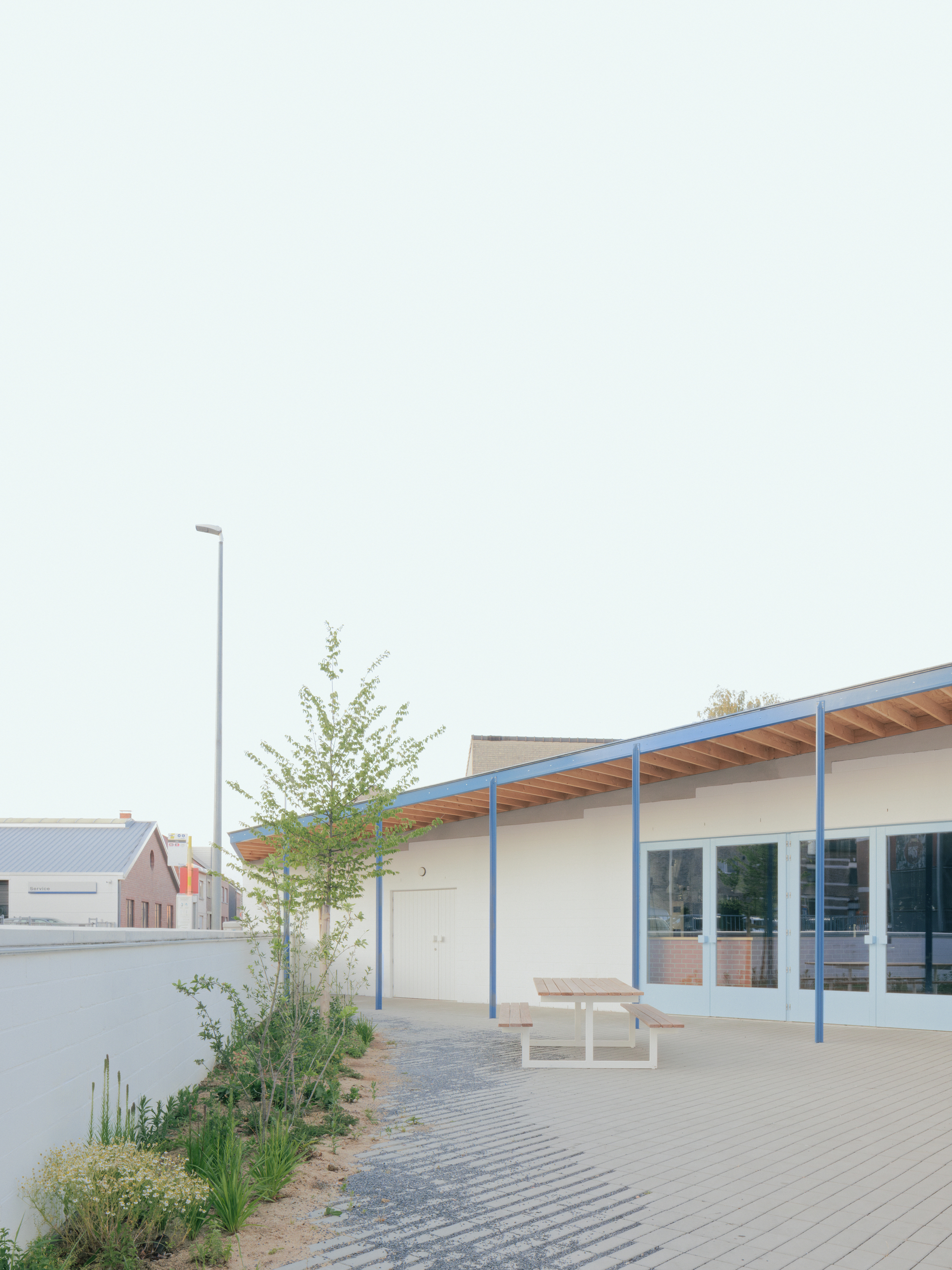 Courtyard with paver surface, timber picnic tables and planted beds beneath the overhanging timber and steel roof