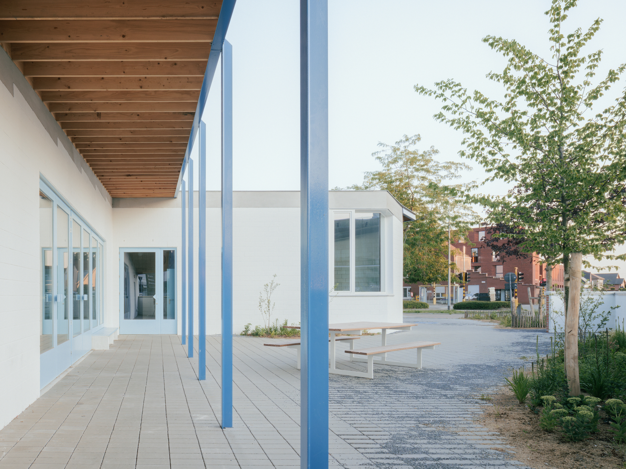 Covered walkway with timber decking and exposed wood ceiling supported by slender blue steel columns
