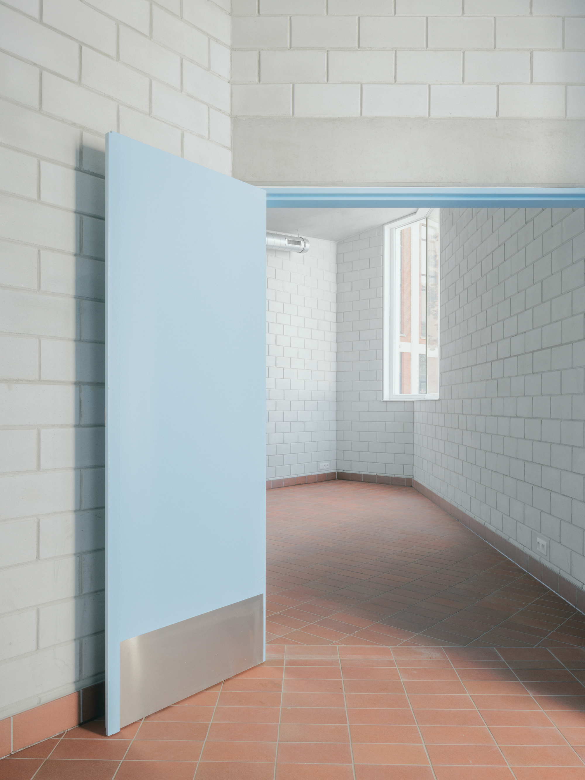 Interior room with white subway tile walls, terracotta floor and partially open pale blue door