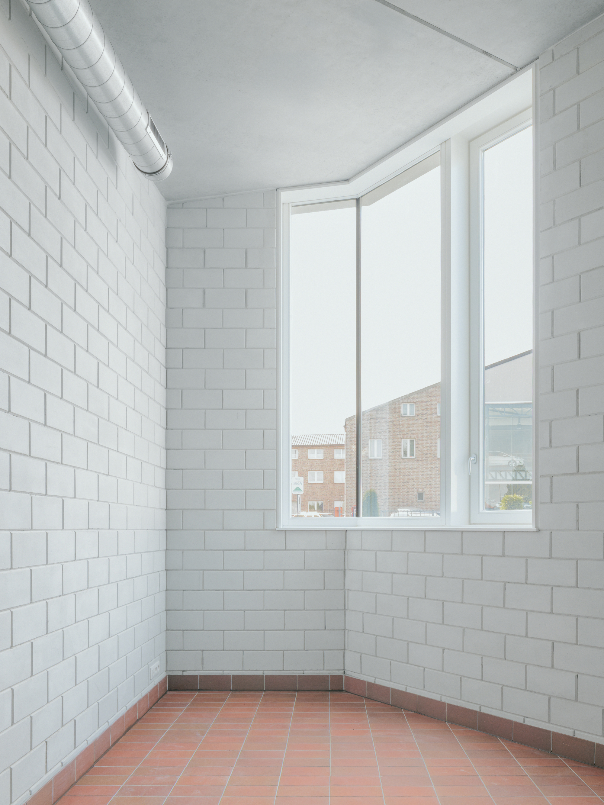 Corner room with white tiled walls, exposed ductwork and corner window overlooking neighboring buildings