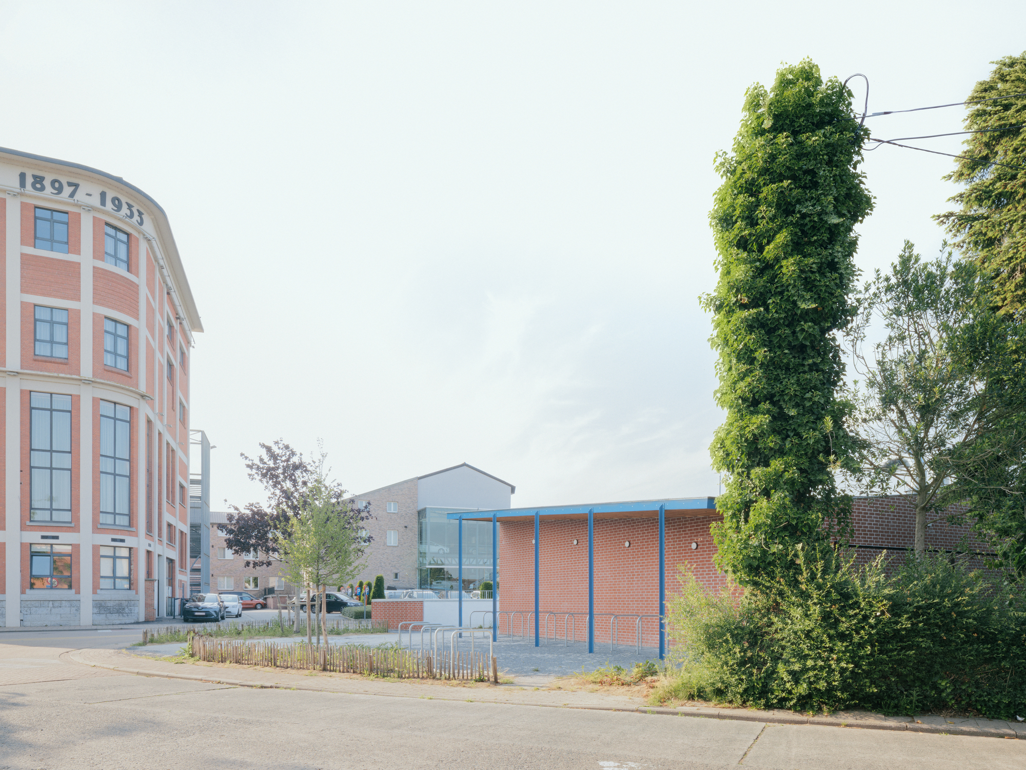 Street view of brick pavilion with blue trim beside curved facade and trees