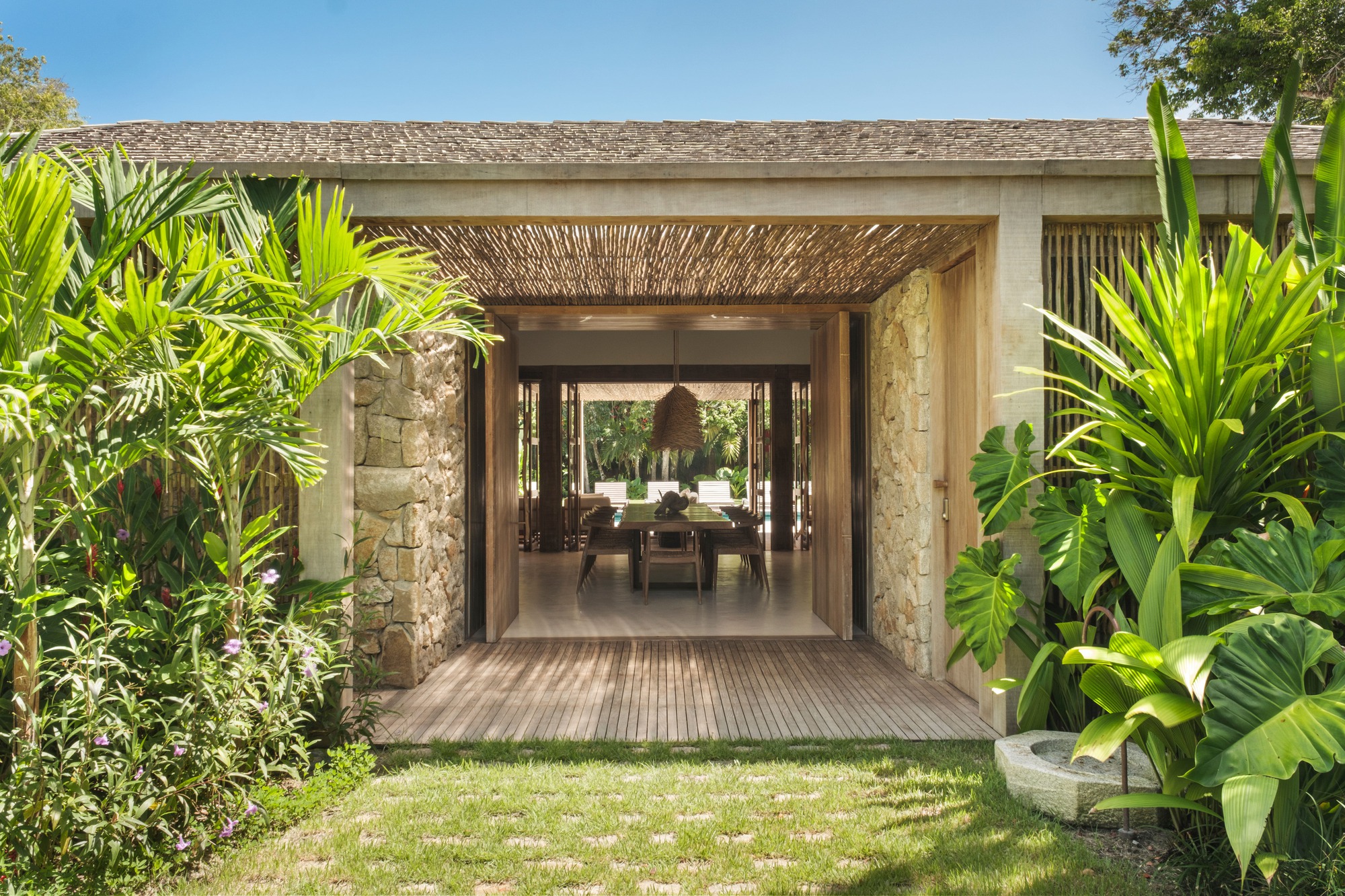 Garden approach through lush tropical planting to covered entry passage with woven timber ceiling screen