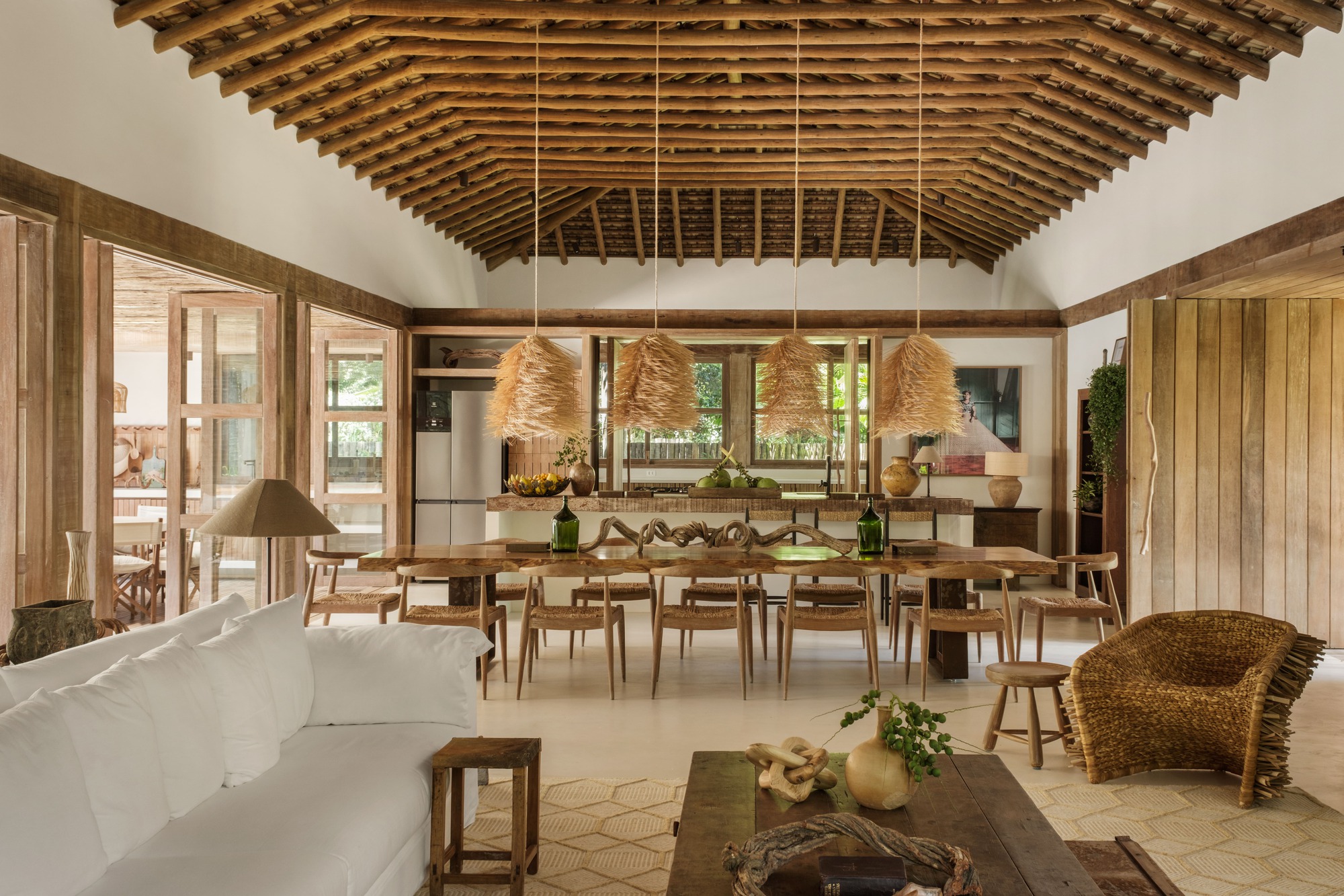 Open plan dining and living area beneath exposed timber rafters with woven pendant lights overhead