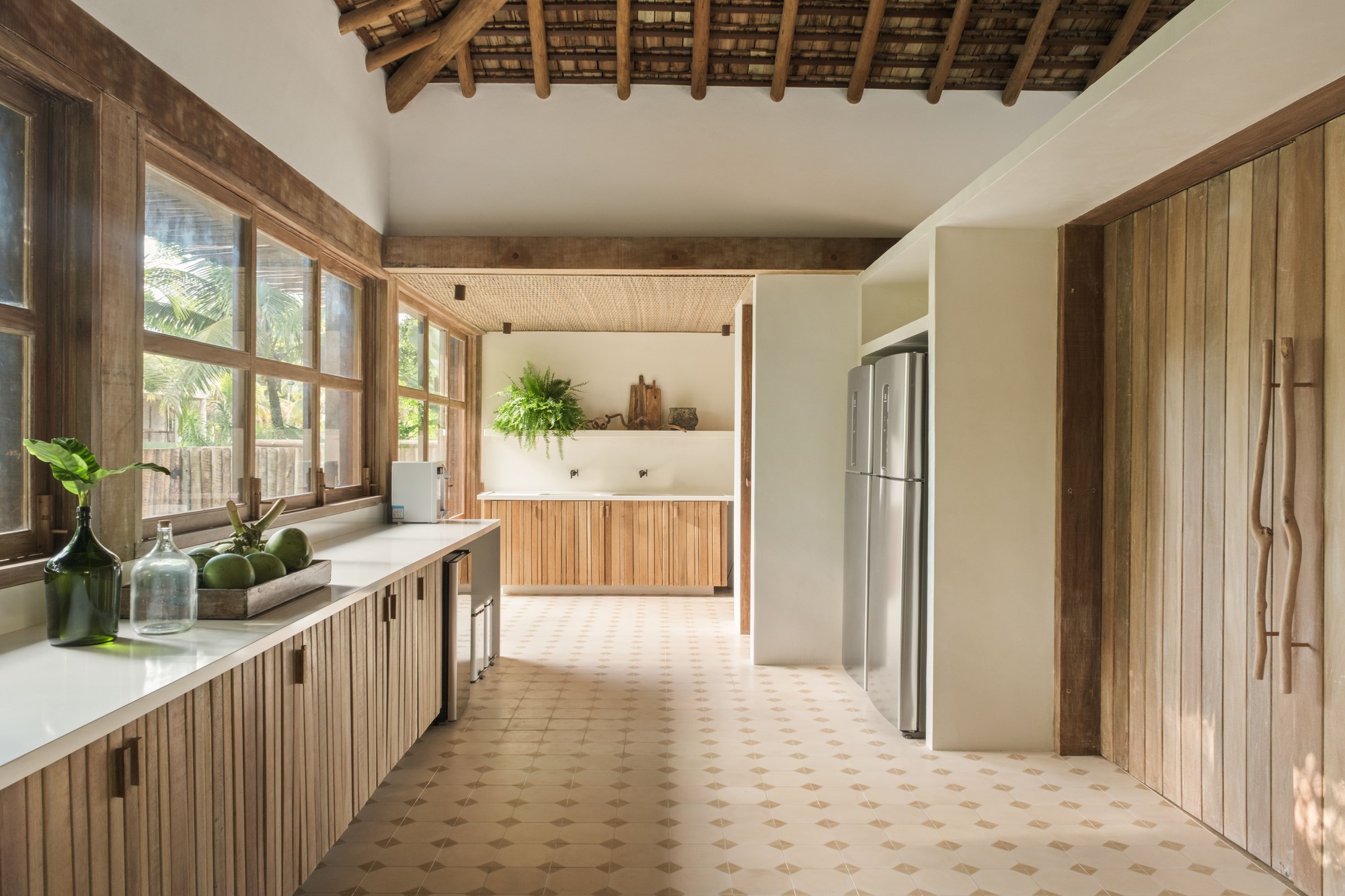 Kitchen passage with patterned terracotta floor tiles and vertical timber-clad cabinetry under exposed rafters