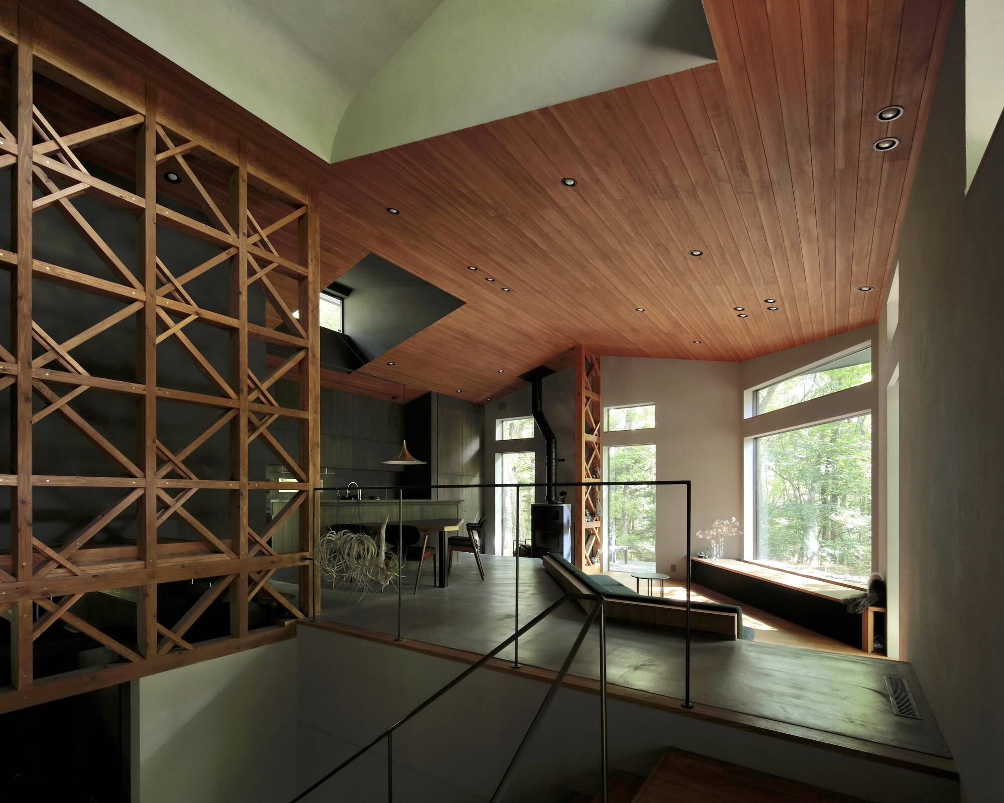 Glass-railed mezzanine overlooking main living space with diagonal lattice screen and forest views