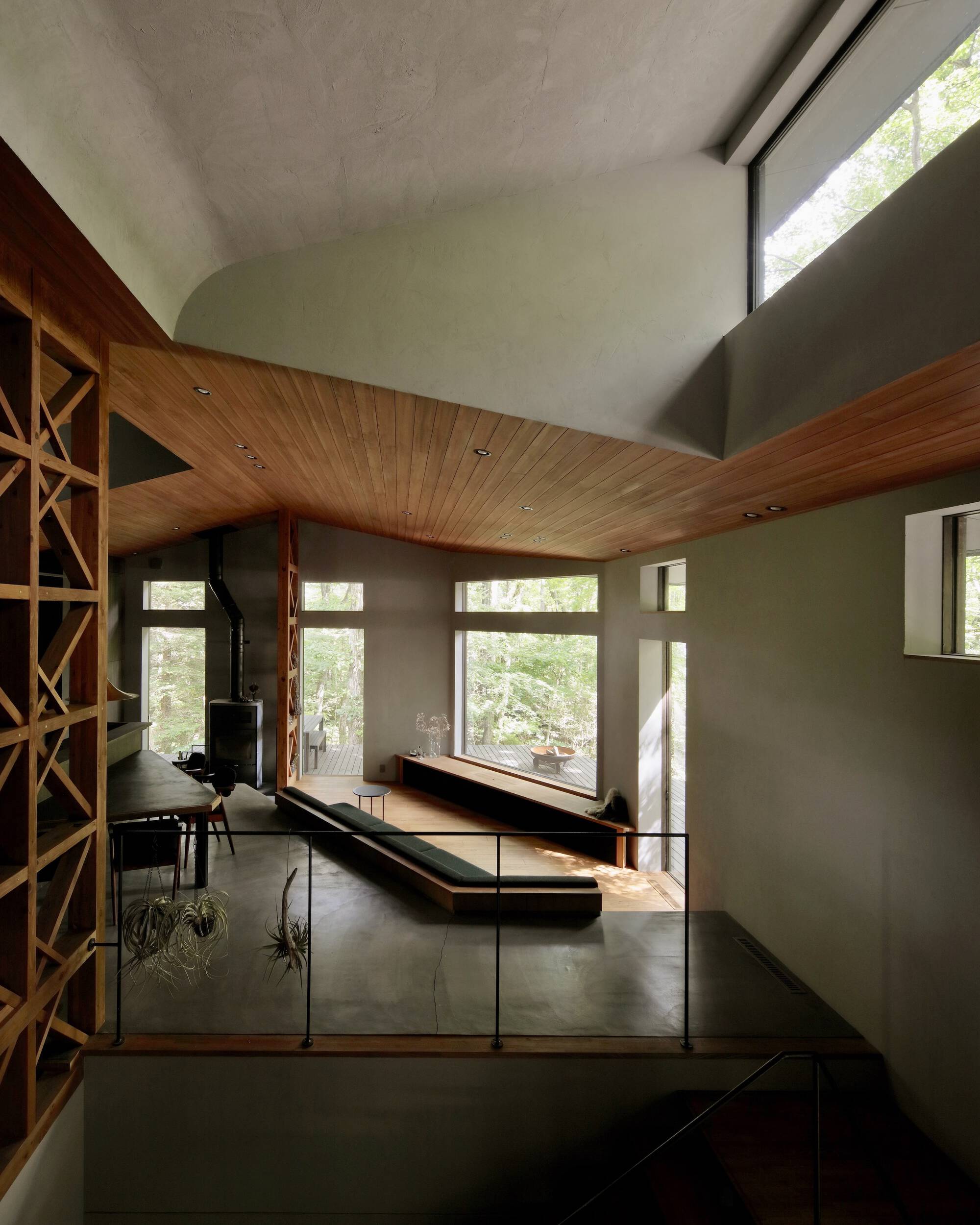 Double-height living space with wood slat ceiling and glass railings overlooking the forest