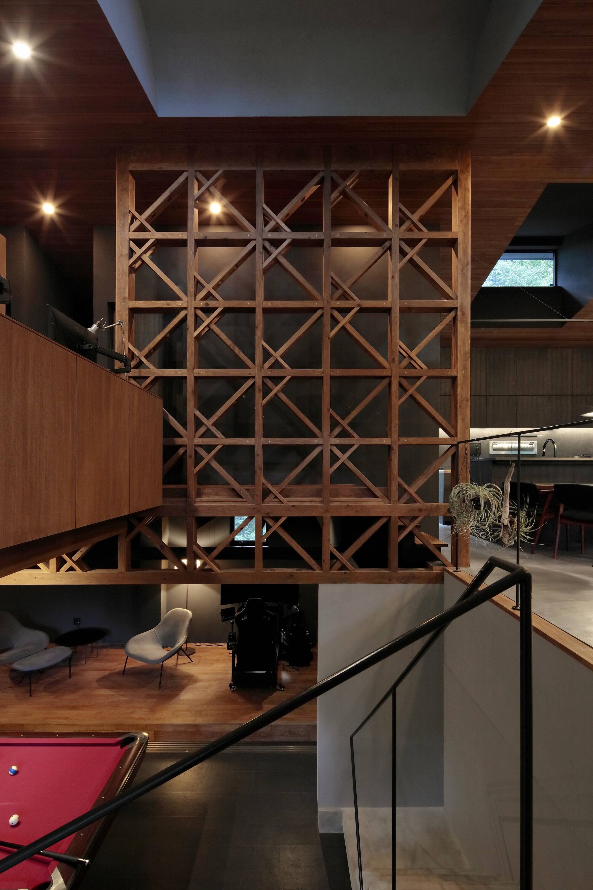 Double-height interior showing a freestanding timber lattice screen between wood-clad mezzanines under recessed lighting