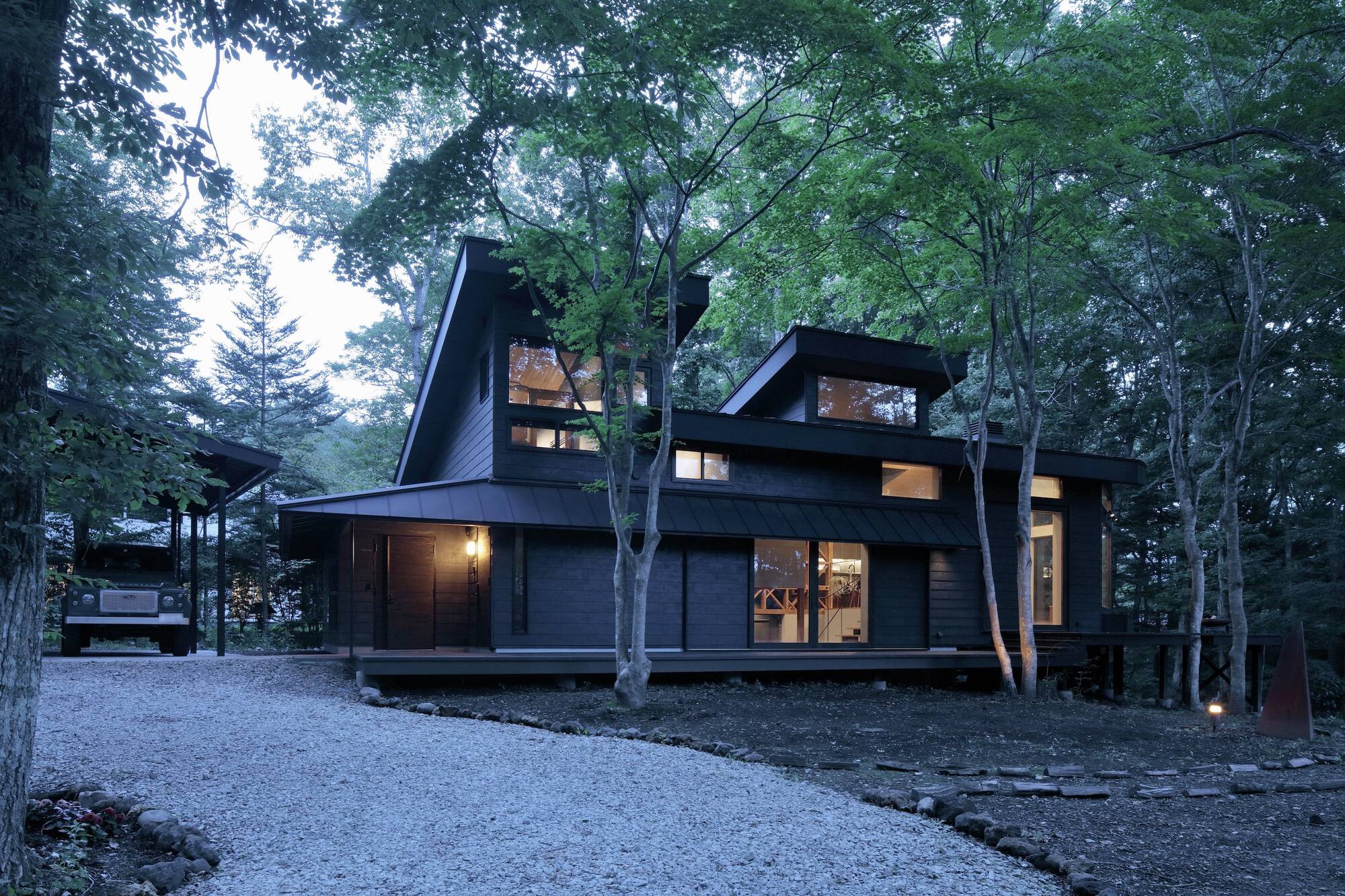 Dark wood-clad volumes with angled rooflines nestled among birch trees at dusk