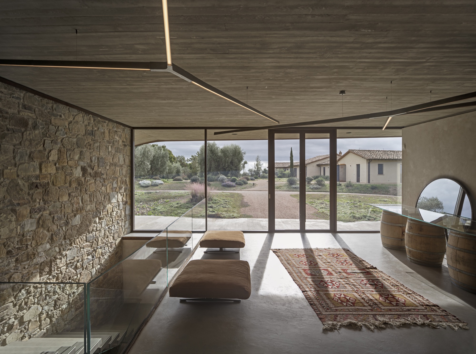 Interior tasting room with stone wall, timber ceiling, linear lighting, and glazed doors framing the landscape