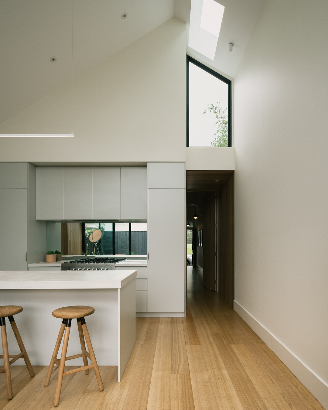 Kitchen island with pale cabinetry beneath a skylight and clerestory window looking toward the hallway