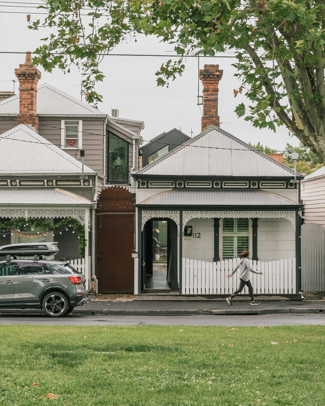 Street facade of a Victorian cottage with white corrugated roofing and a pedestrian crossing the footpath