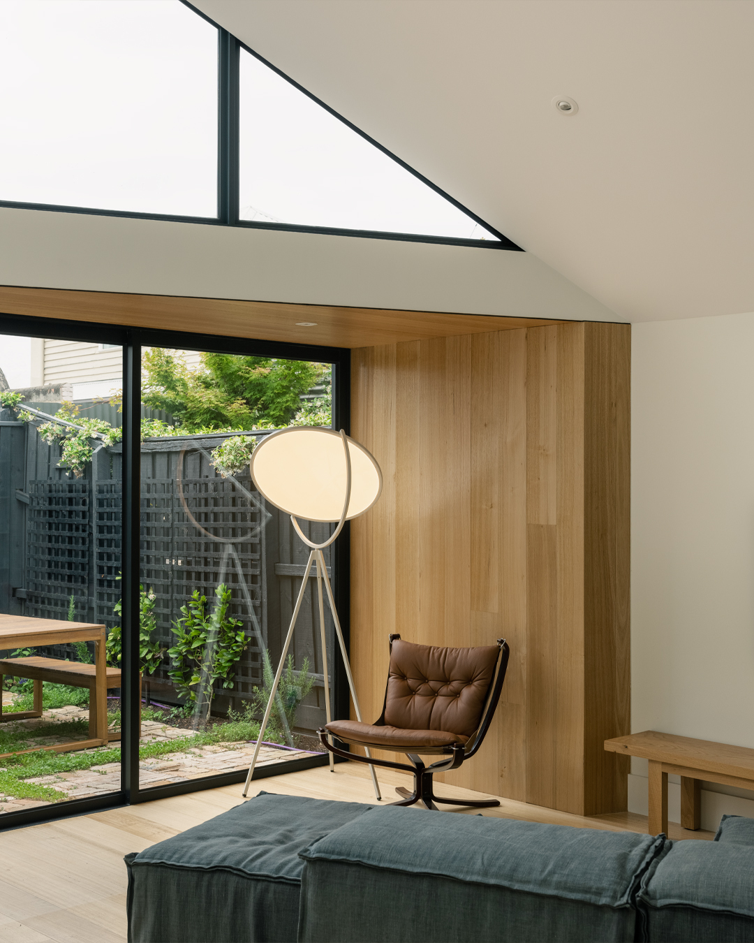 Timber-paneled wall beside the glazed door with triangular clerestory window overhead admitting daylight