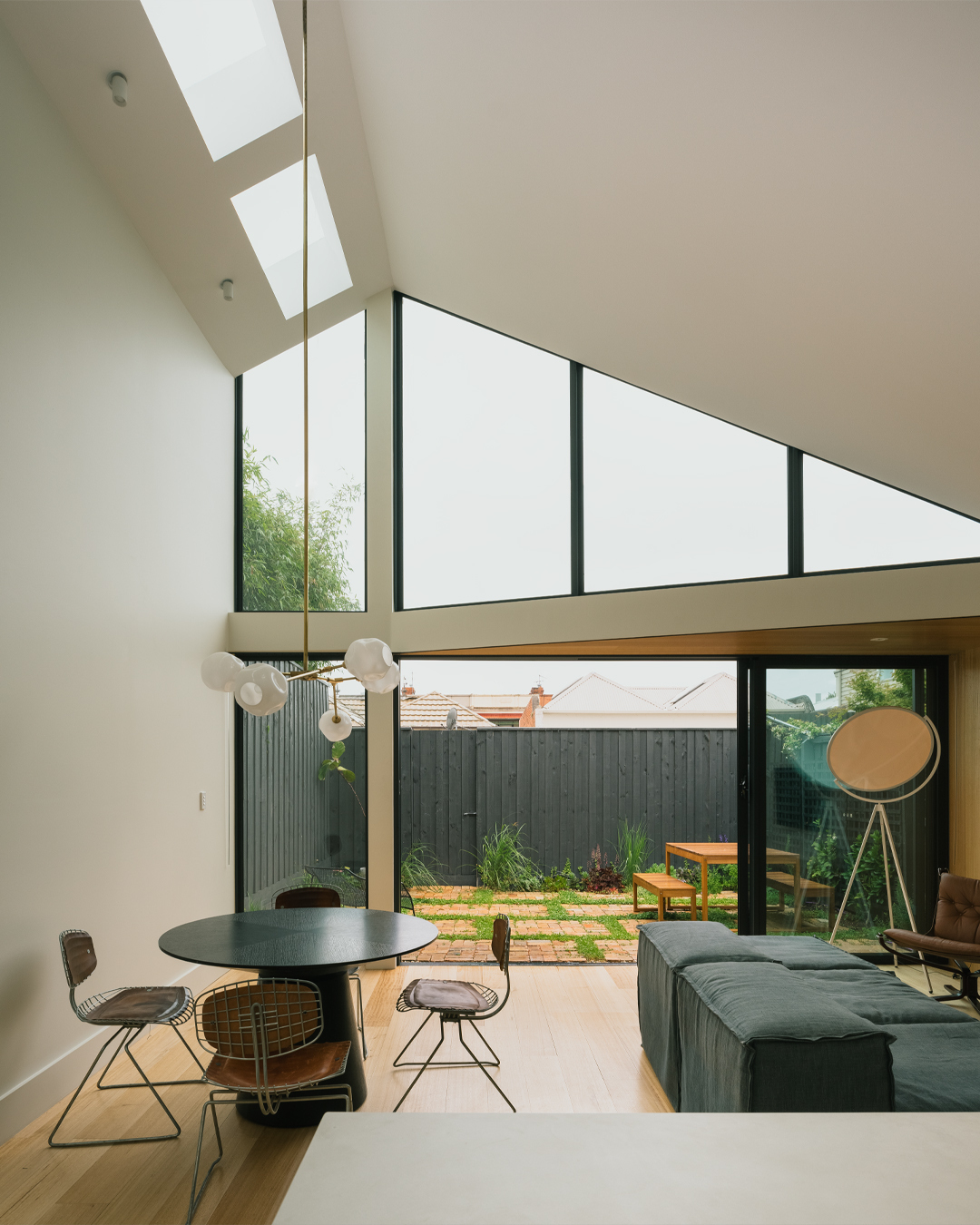 Double-height living space with angled skylights and full-height glazing opening to a courtyard with timber pavers