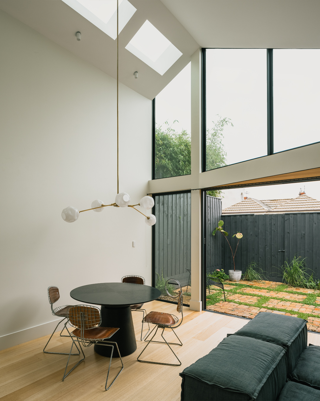 Dining area beneath clerestory windows and square skylights overlooking a planted courtyard with corrugated fence