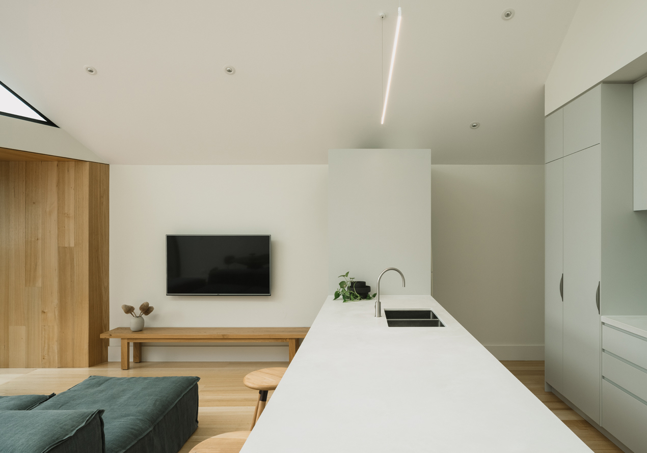 White stone kitchen island with integrated sink facing timber joinery and flat-screen television on wall