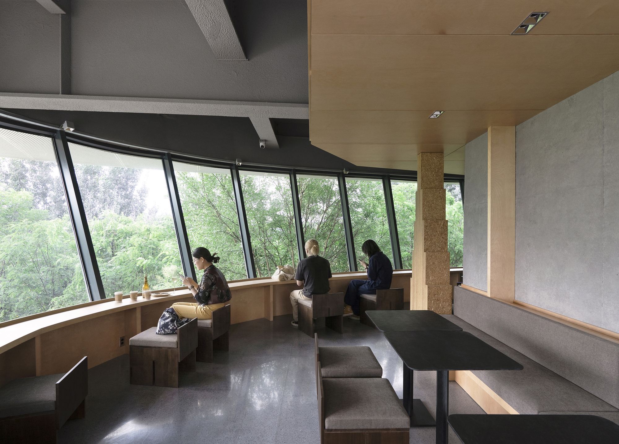 Seating alcove with angled windows overlooking greenery and three visitors at built-in benches