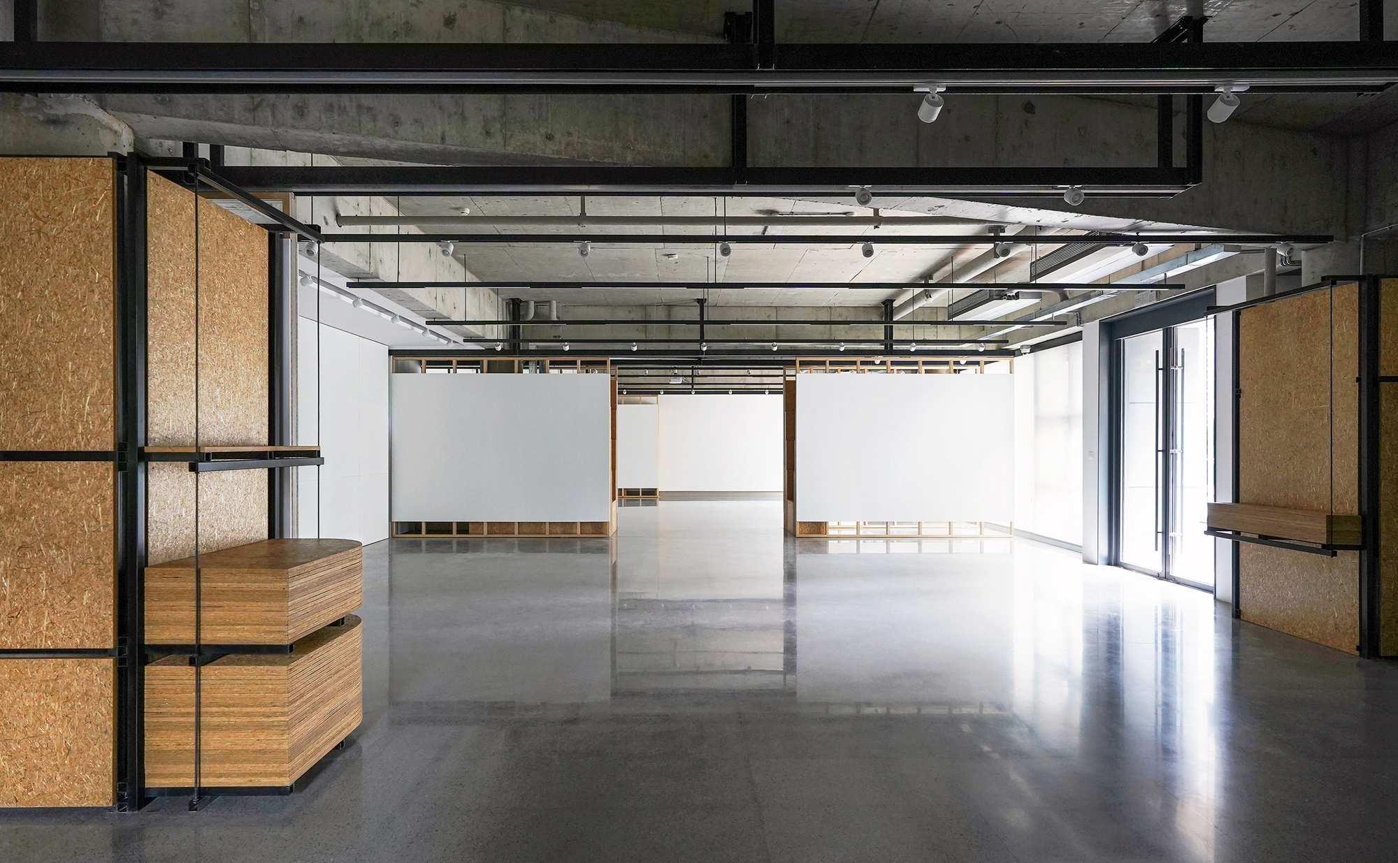 Open interior space with exposed concrete ceiling, steel beams, and modular timber and OSB partition walls
