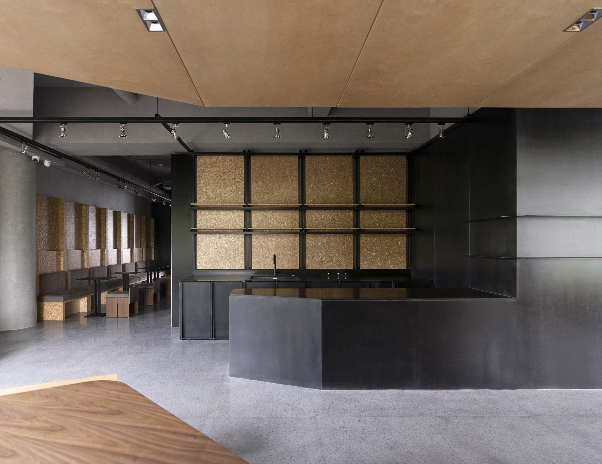 Reception desk in blackened steel with cork-paneled wall grid and track lighting above