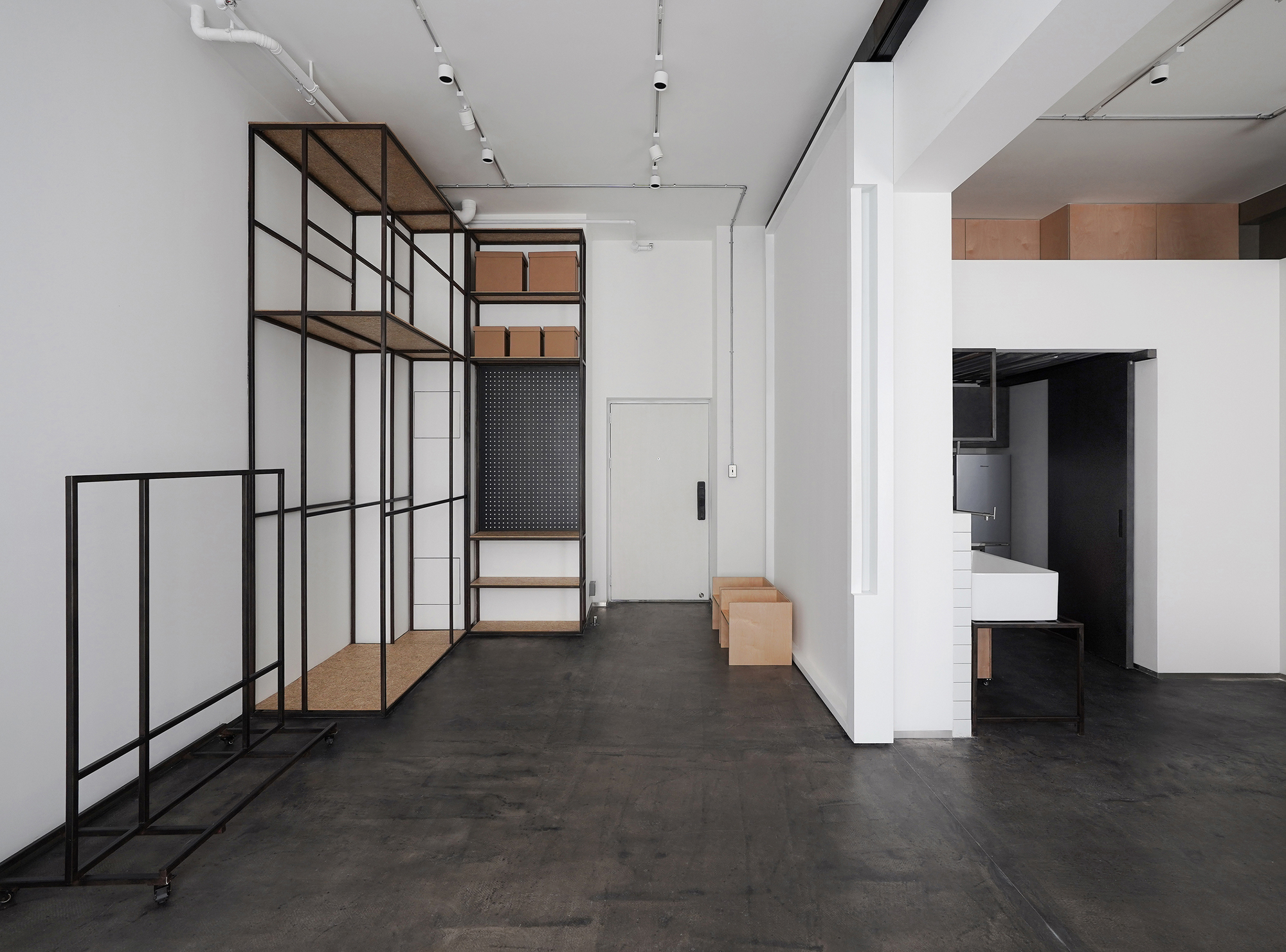 Corridor with freestanding black metal shelving unit holding timber boxes alongside white service core