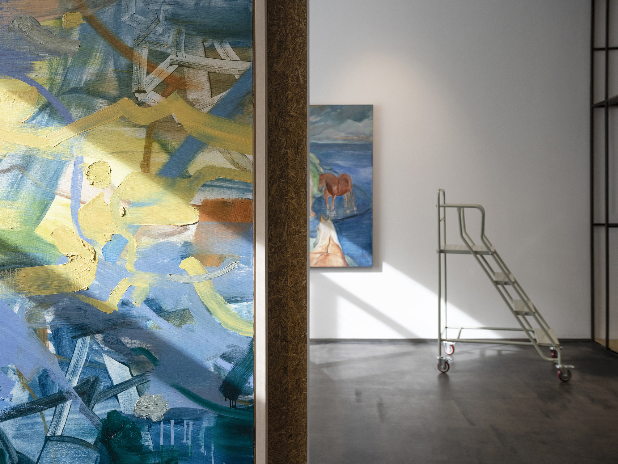 Gallery interior with abstract paintings on white walls and a metal rolling ladder on polished concrete