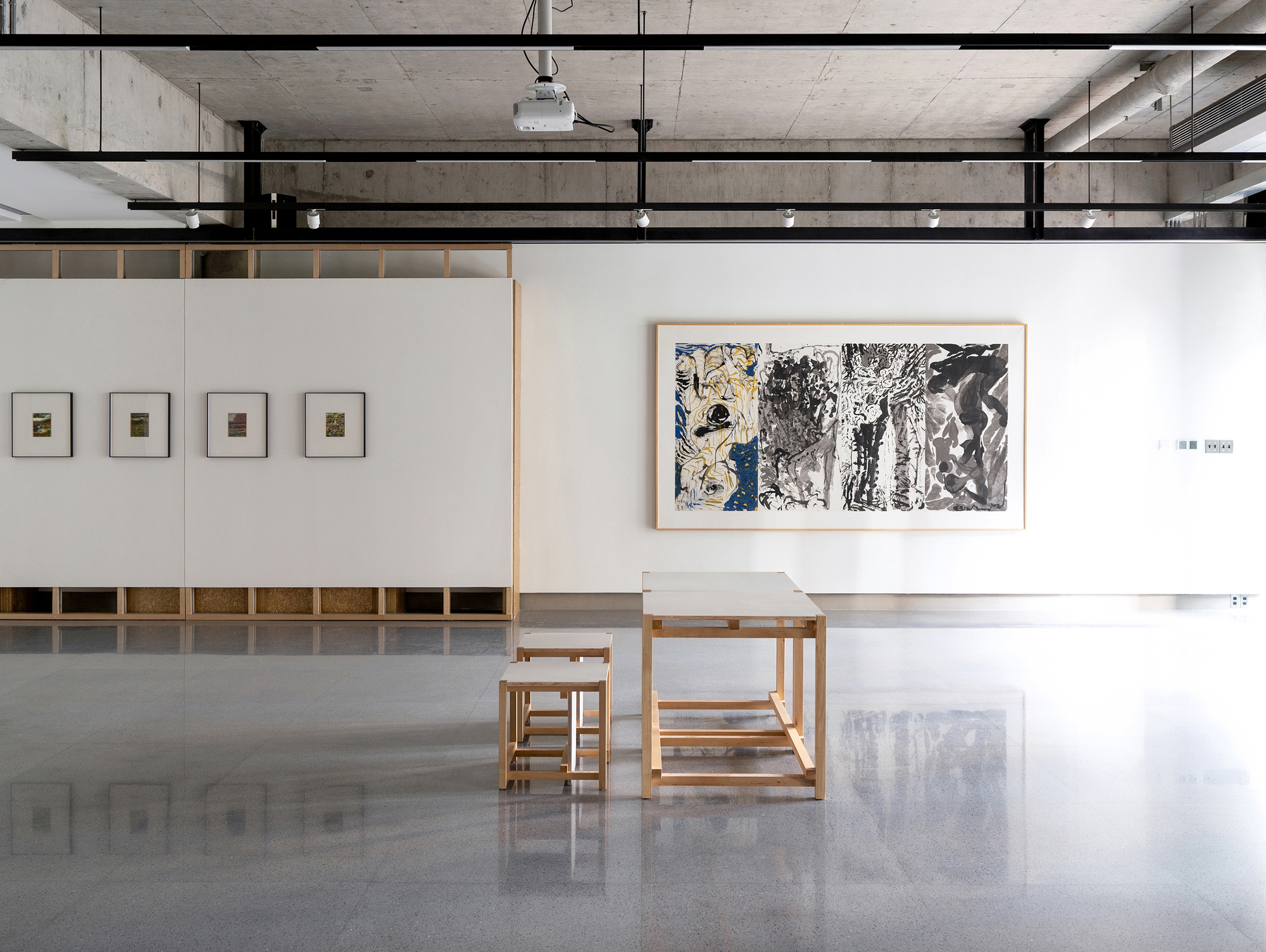 Gallery room with exposed concrete ceiling, timber furniture, and framed artworks on white walls
