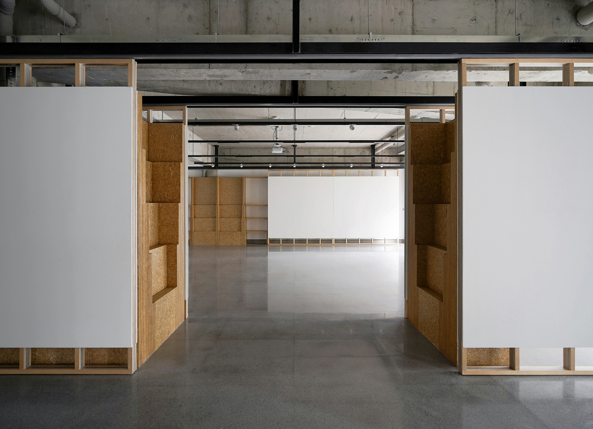 View through doorway framed by cork-paneled walls leading to connected exhibition spaces beyond