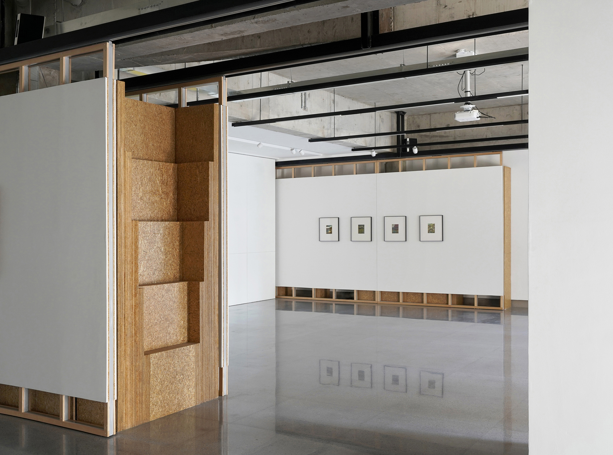Gallery space with movable white partition panels and cork-lined recesses beneath an exposed concrete ceiling