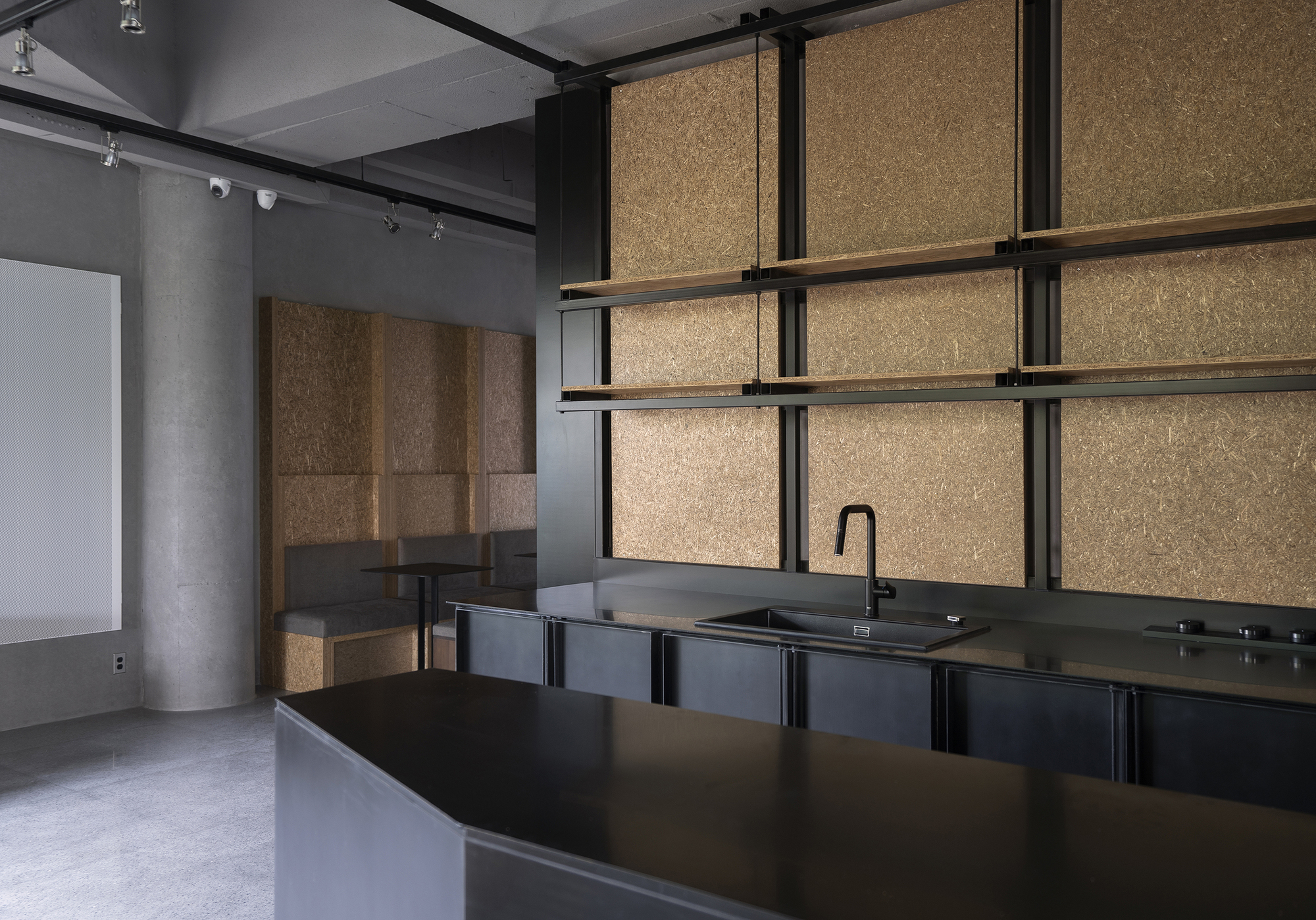 Kitchenette with black metal cabinetry and cork-paneled walls within a gallery support space
