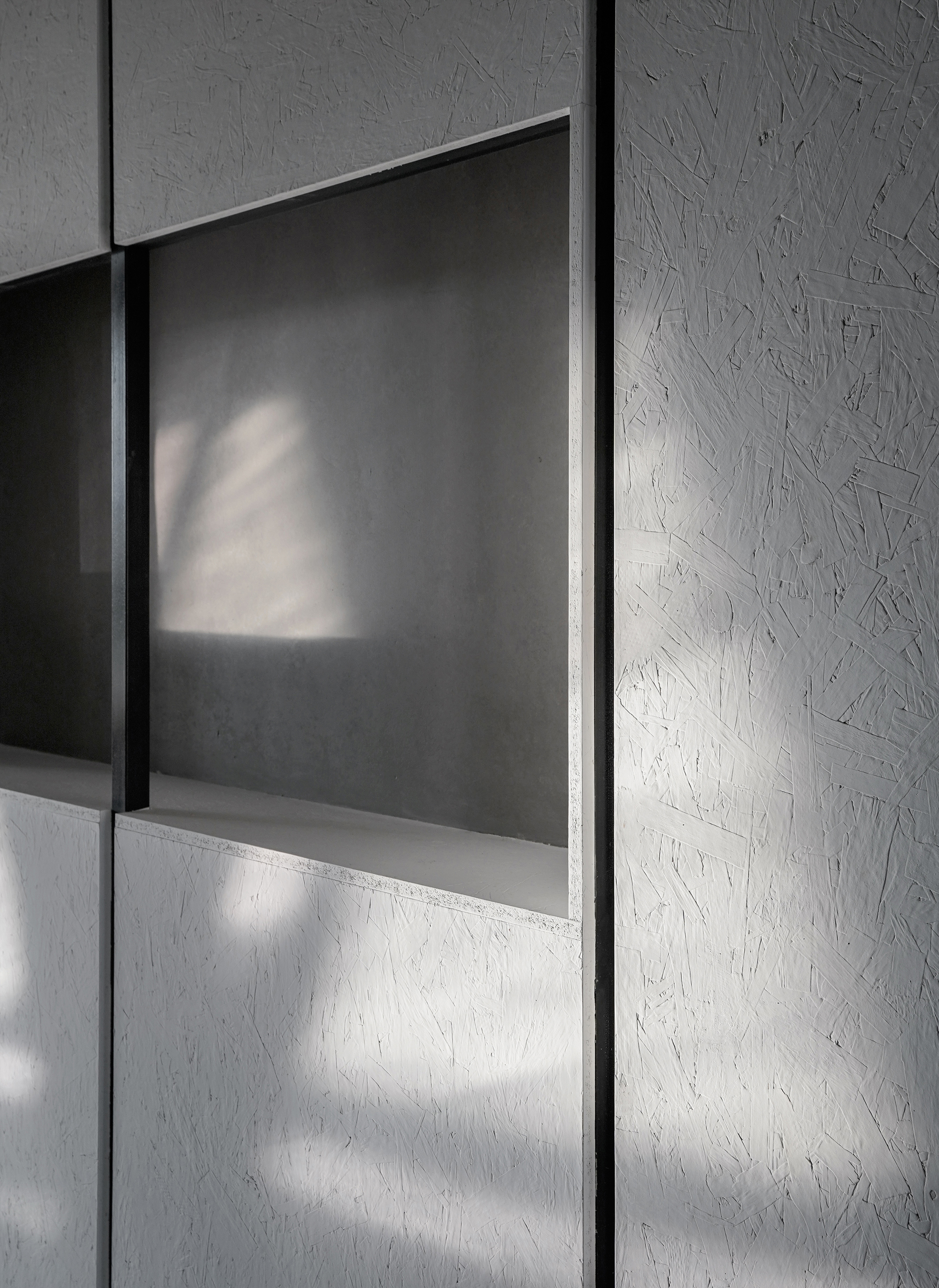 Detail of grey panel wall with recessed opening casting angular shadows in natural light