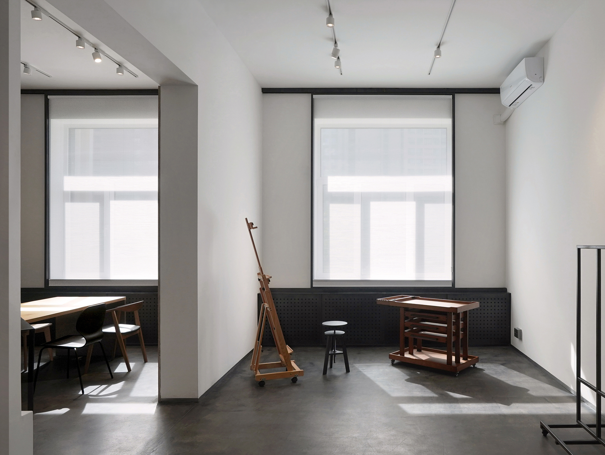 Gallery room with polished concrete floor and wooden easel beside two tall windows with roller blinds