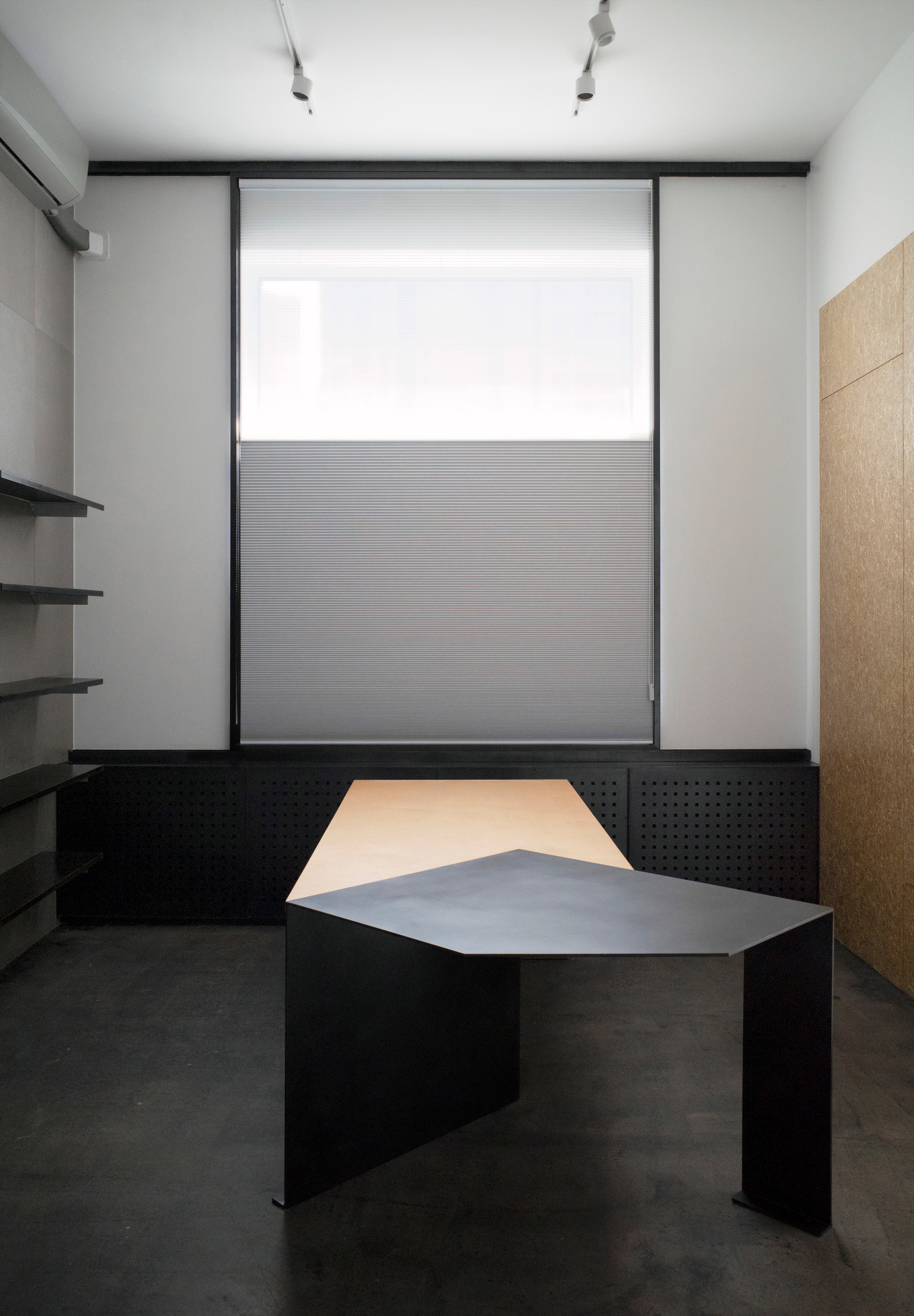 Angular black desk with grey and peach surfaces in a room with white walls and translucent window blinds