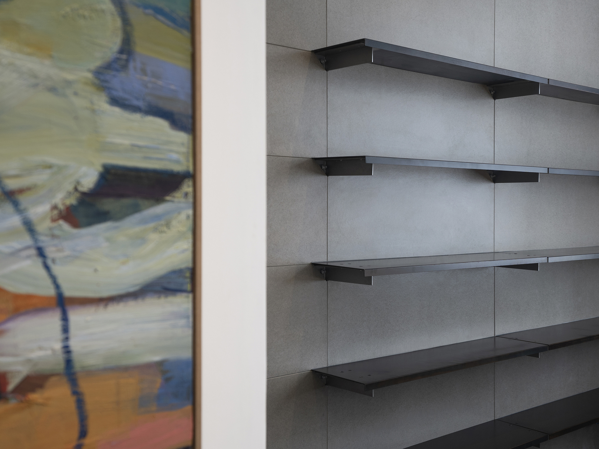 Black metal shelving brackets mounted on grey panel walls beside a framed painting