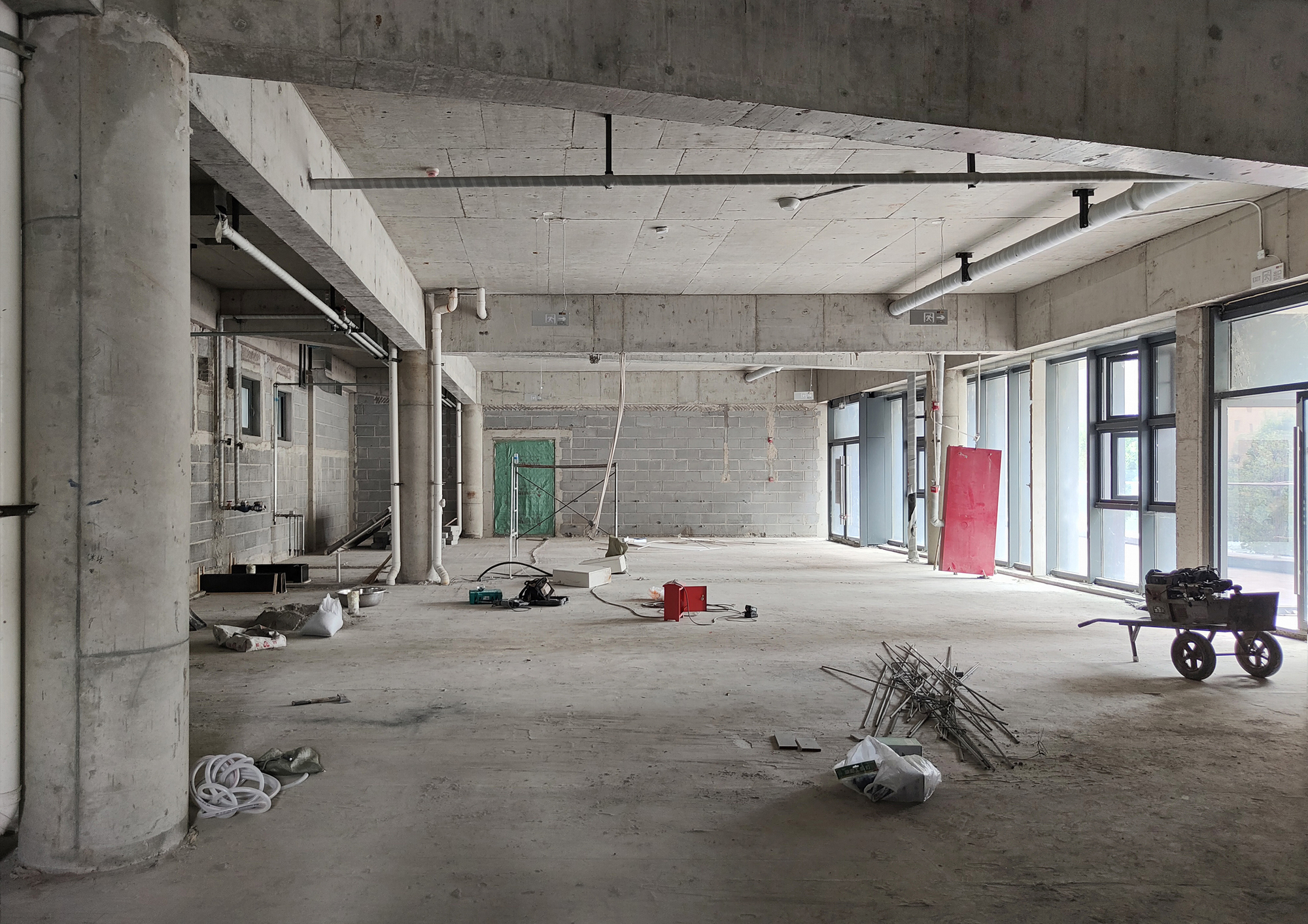 Unfinished concrete interior with exposed columns, beams, and construction materials scattered on the floor