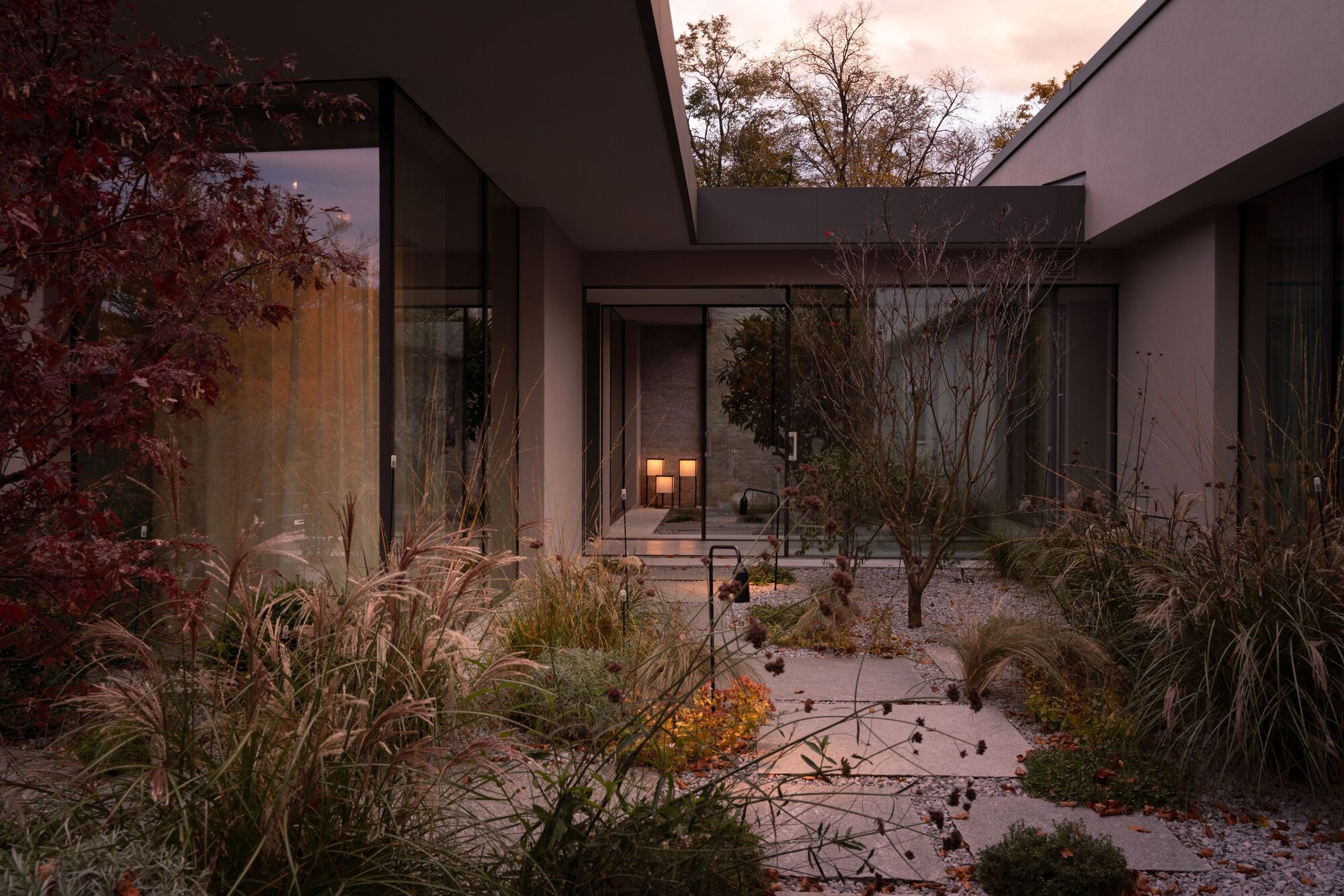 Interior courtyard with gravel bed and native grasses framed by glass walls at dusk