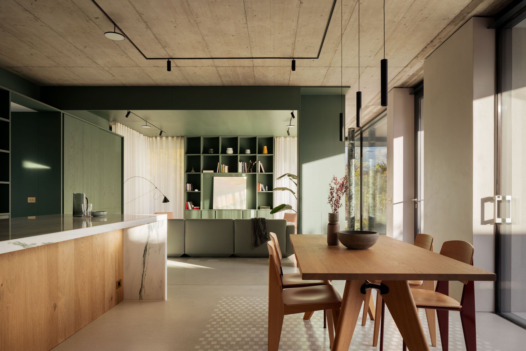 Open kitchen and dining area with exposed concrete ceiling and sage green cabinetry