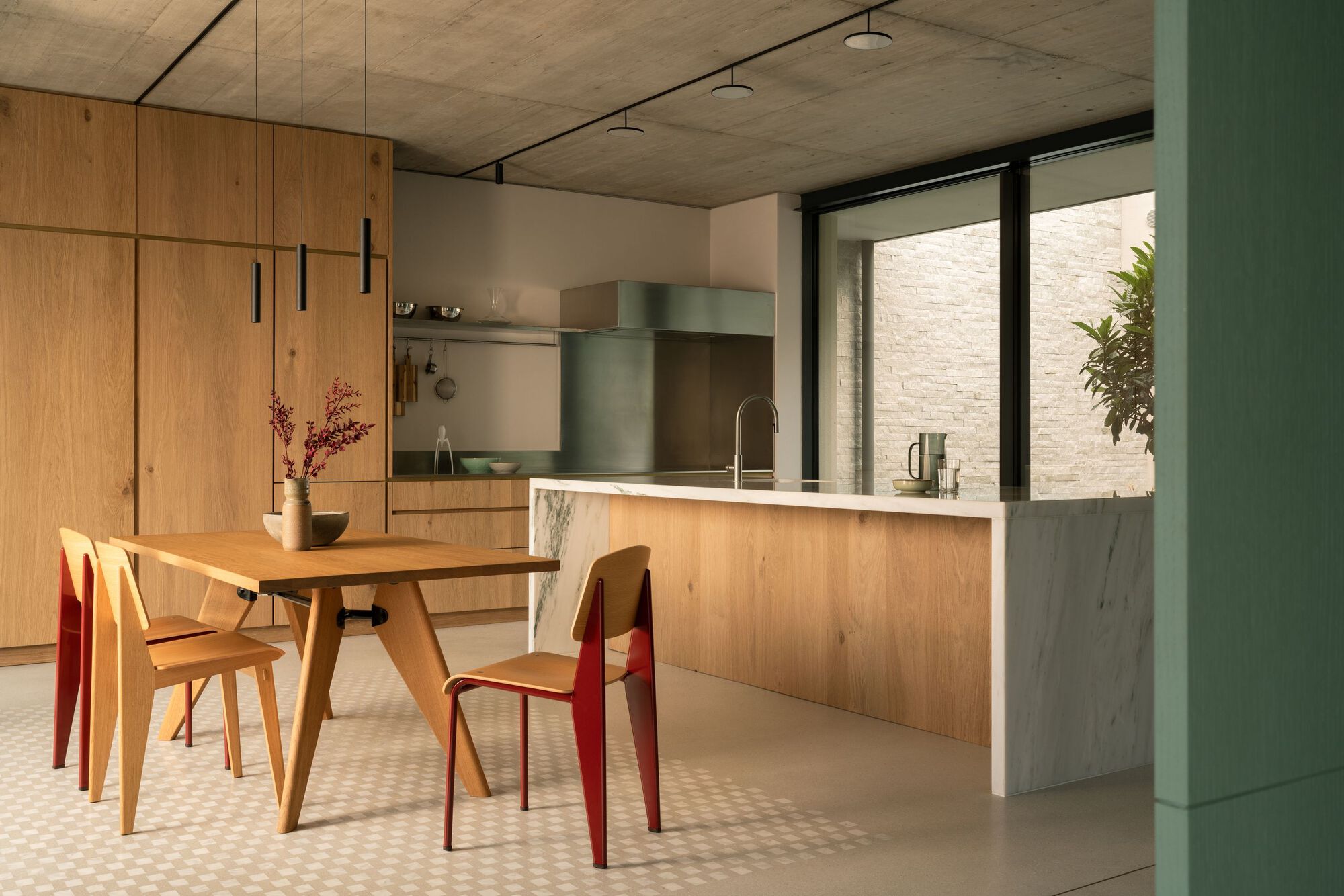 Kitchen island clad in oak and marble under concrete ceiling with morning light