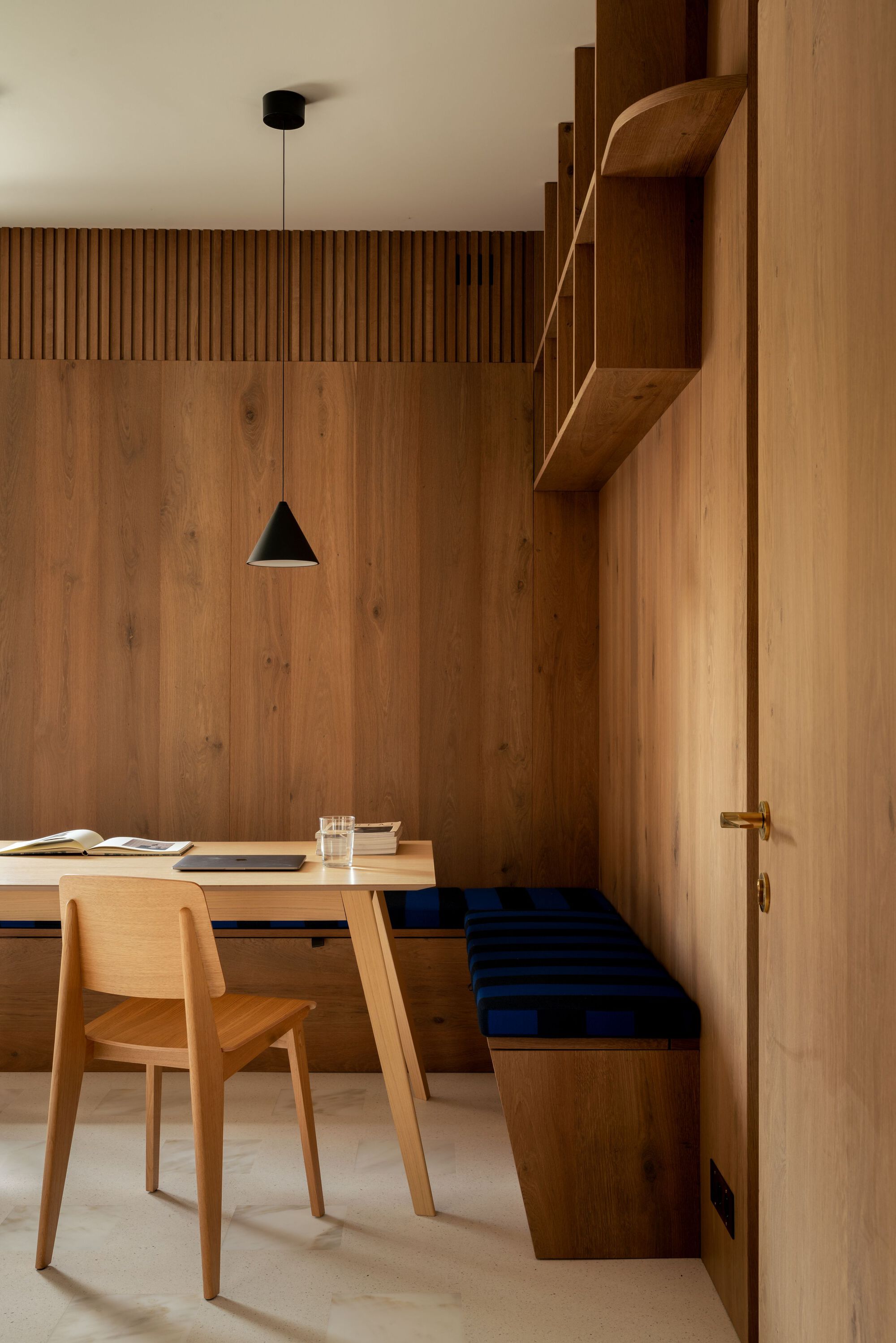 Dining nook with vertical timber paneling, built-in bench with navy cushion, and suspended black pendant