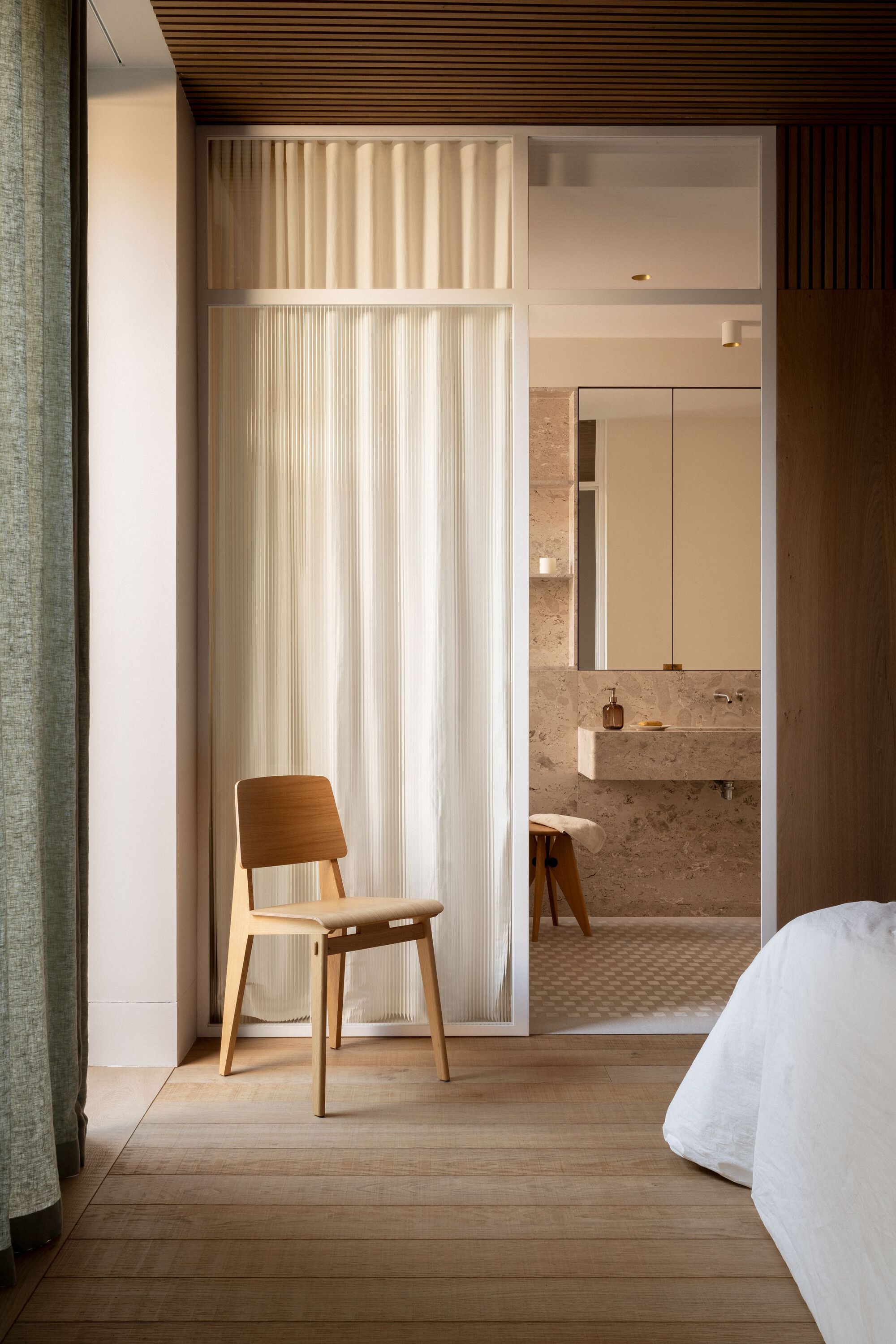 Bedroom threshold with sheer curtain dividing sleeping area from stone-clad bathroom with mosaic floor