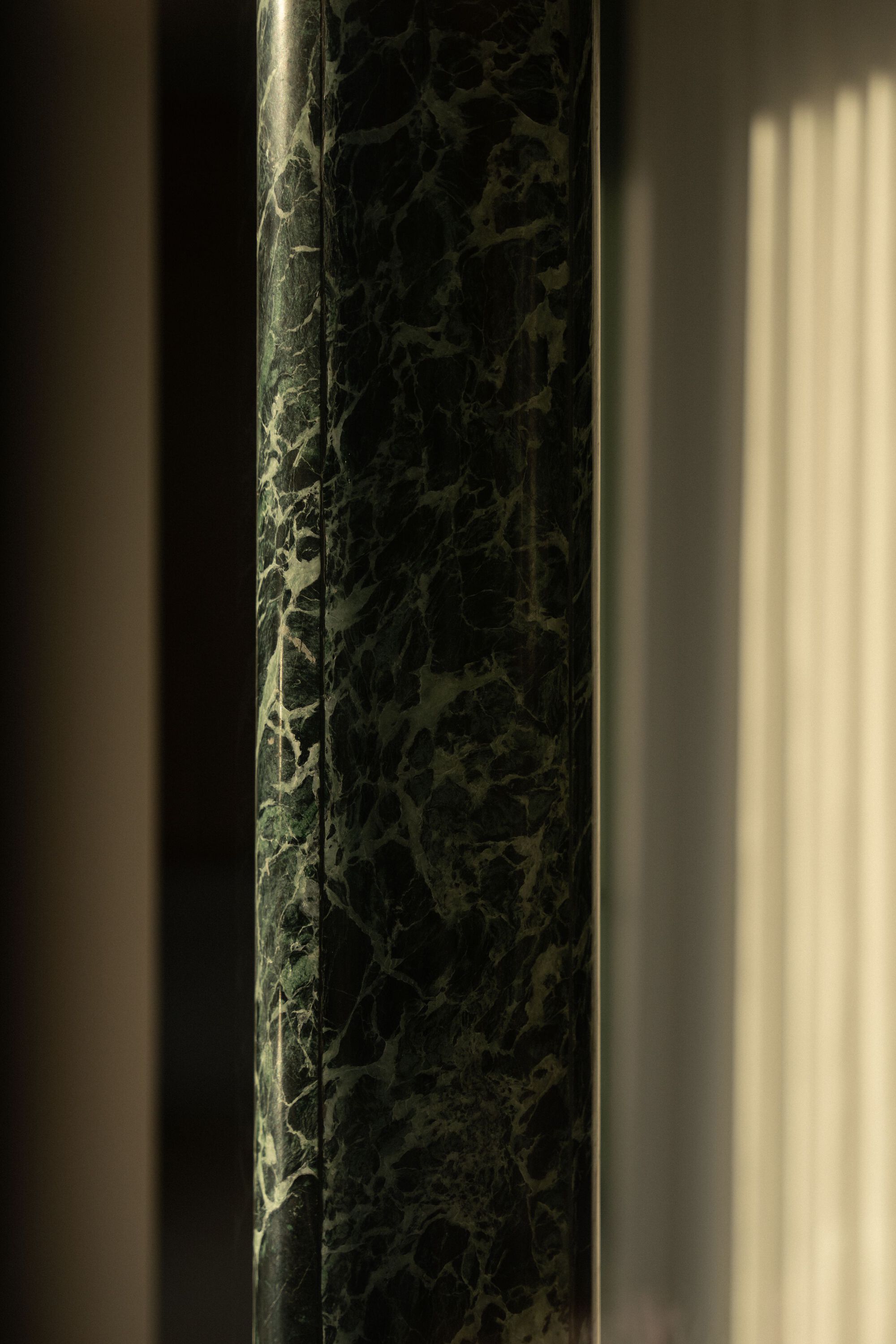 Close-up of a dark green marble column with veining patterns catching afternoon light
