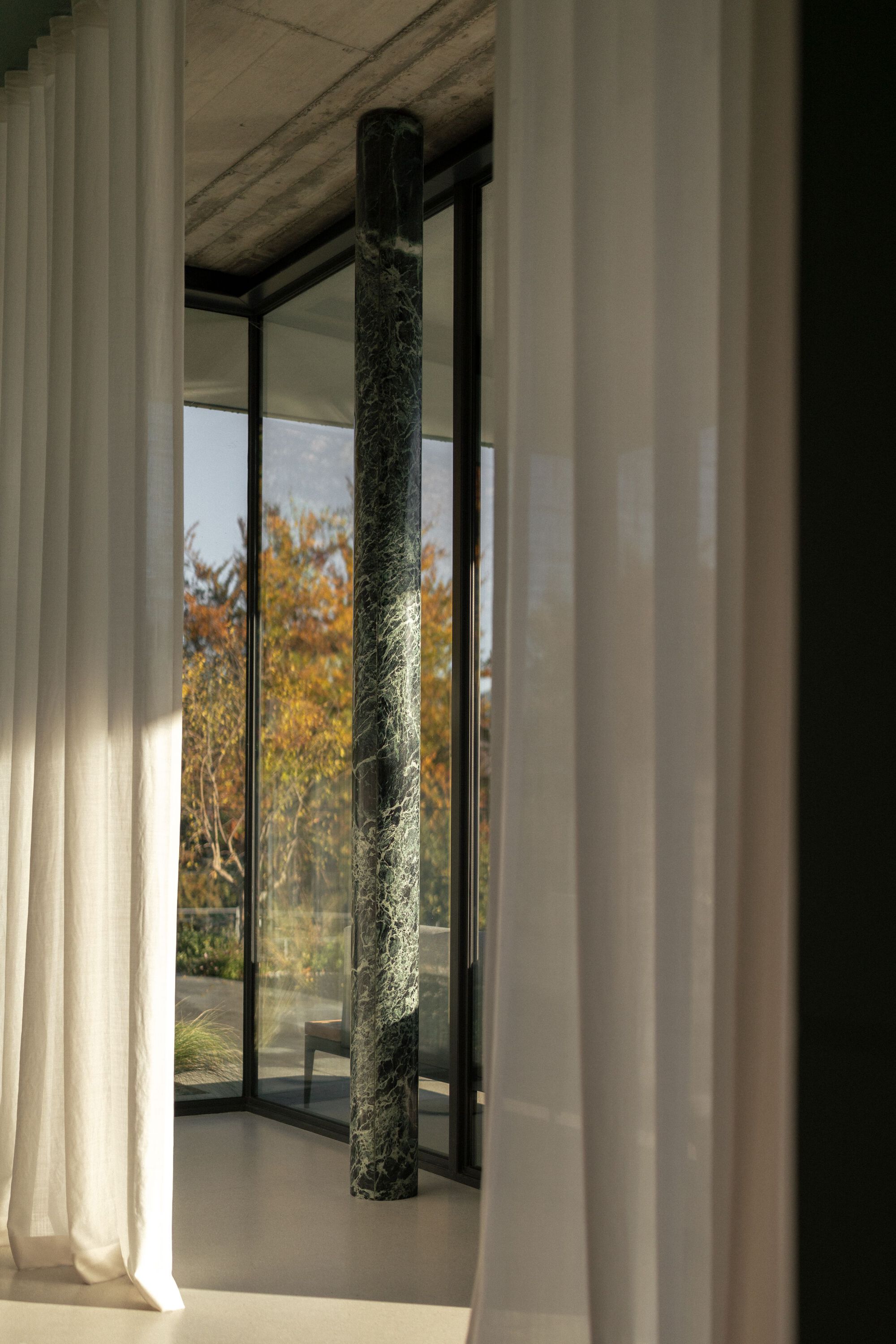 Interior view through sheer curtains to a dark marble column and glazed courtyard in autumn