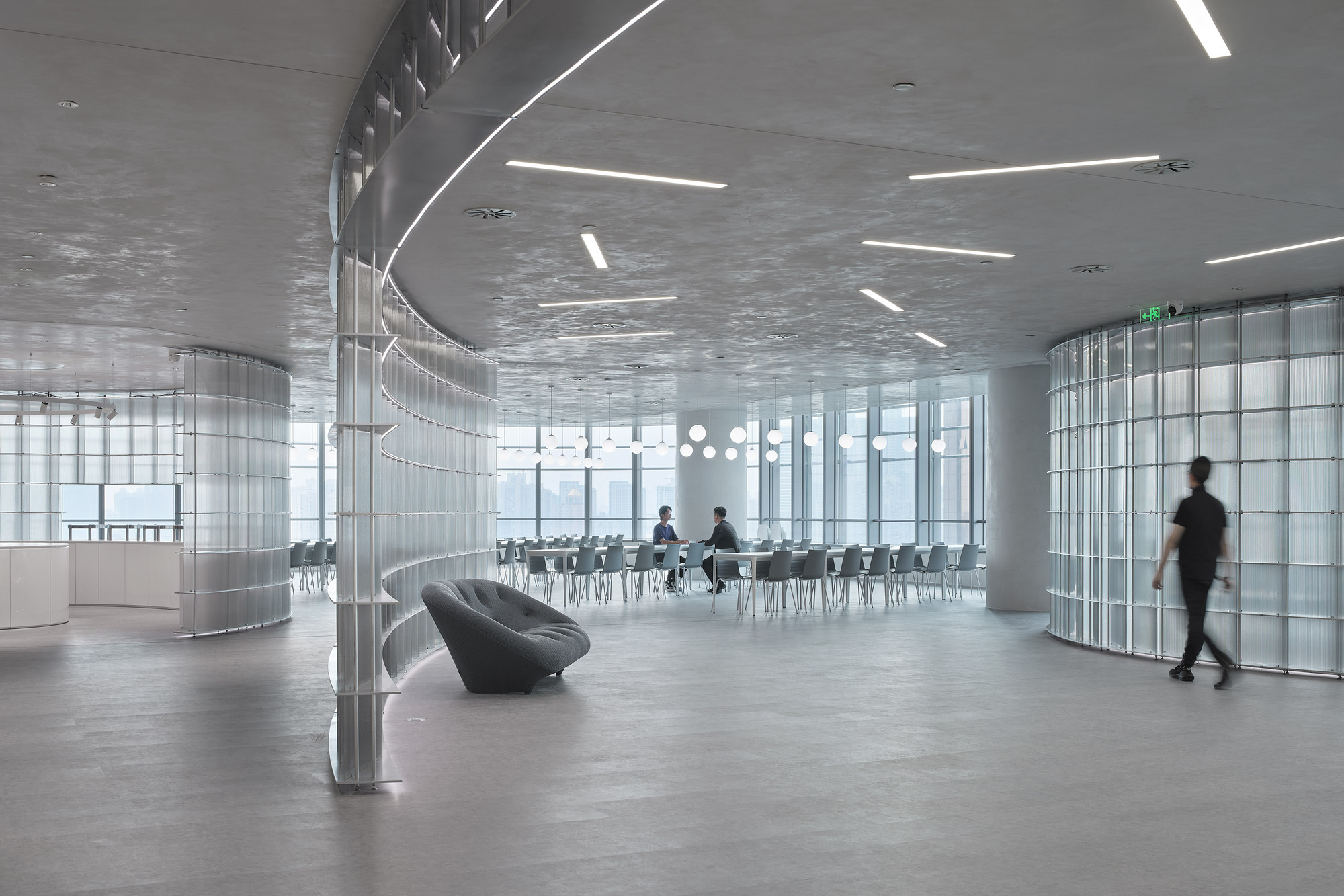 Open office floor with translucent glass block walls and a figure passing by a curved lobby