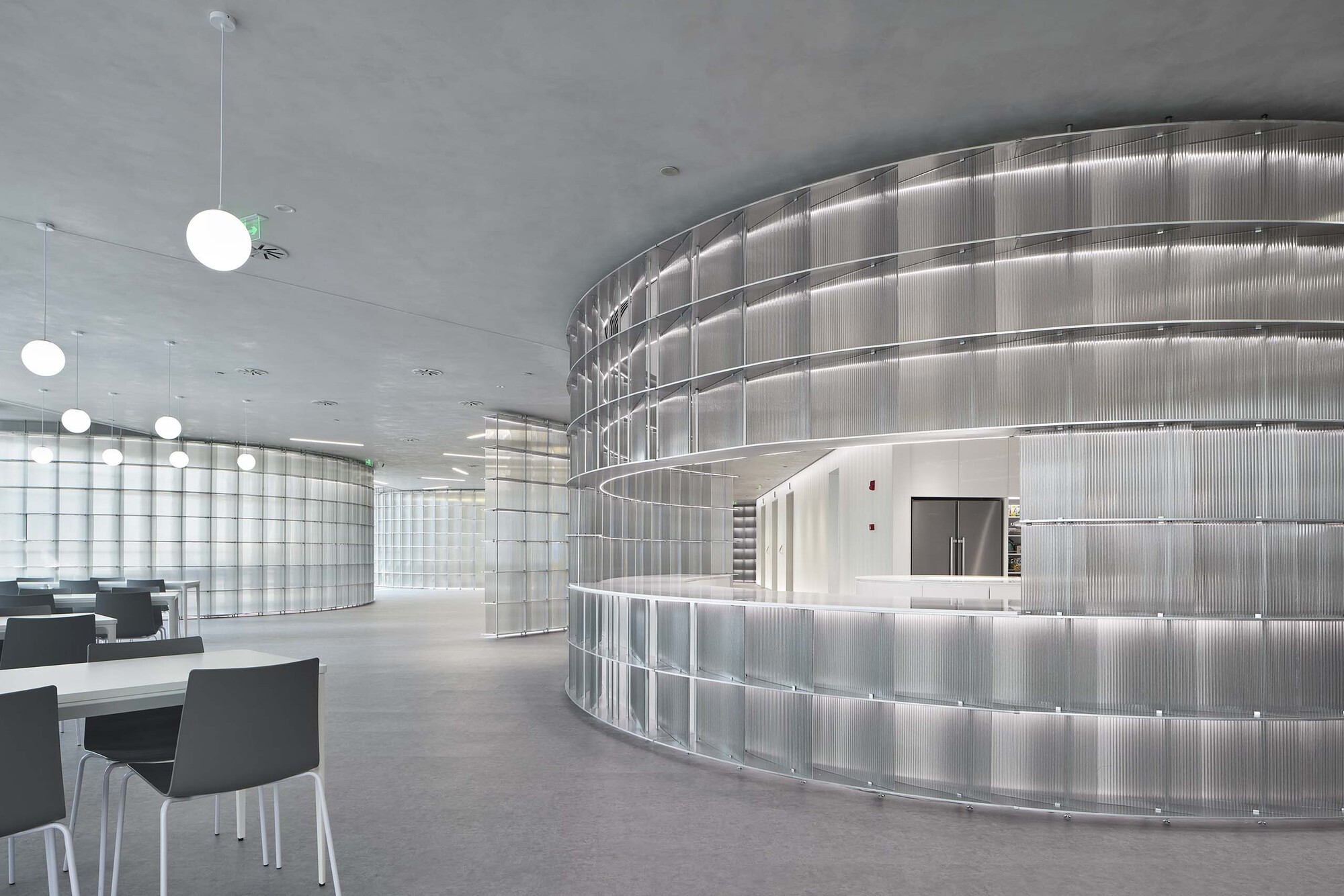Curved reception desk wrapped in backlit glass block panels with pendant globe lights above