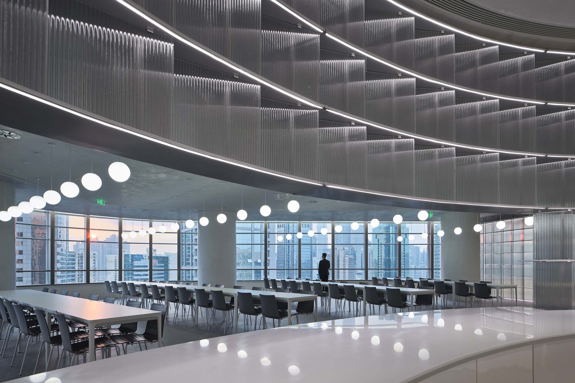 Cafeteria space with ribbed metal ceiling panels, linear lighting, and pendant globes reflected on polished floor